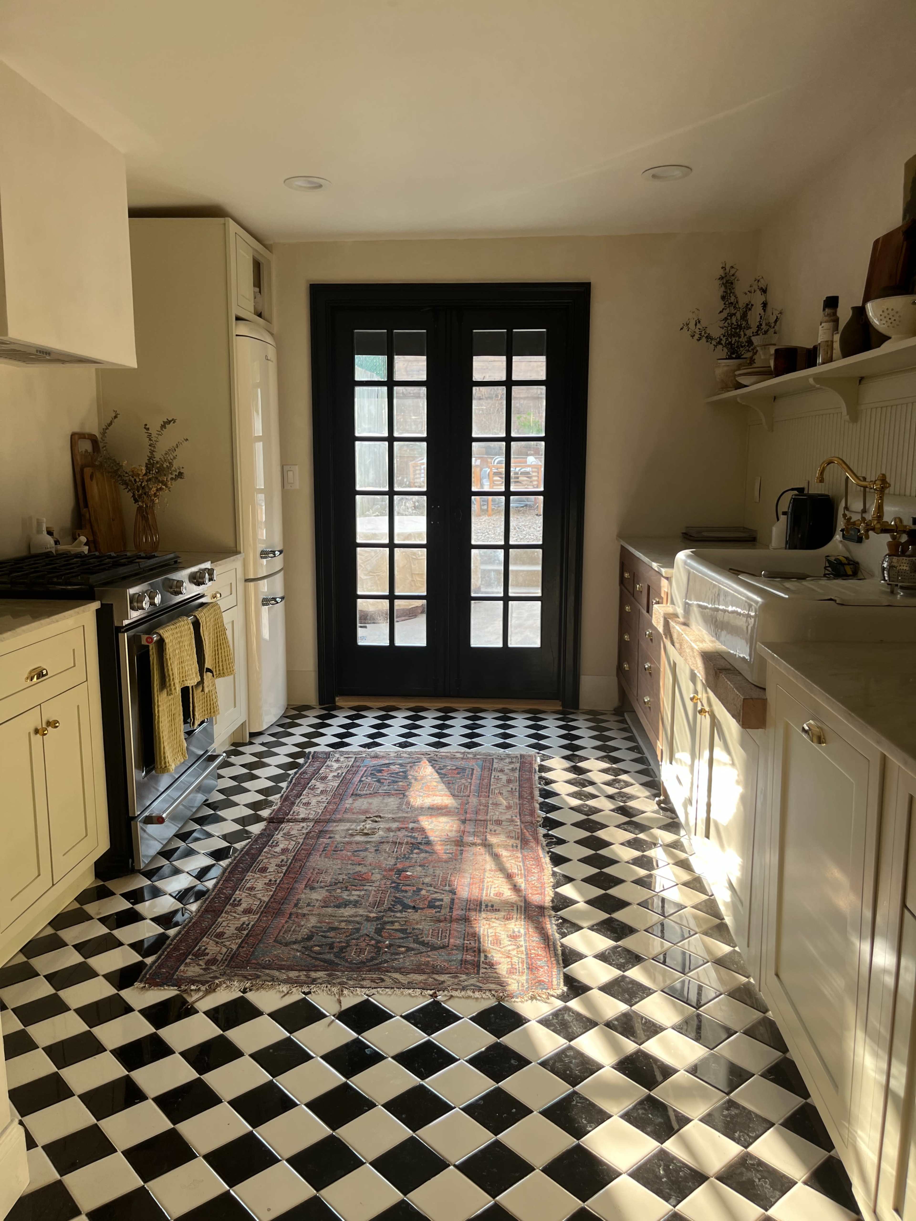 The image shows a kitchen with black and white checkered flooring, a modern stove, and double doors that open to an outdoor area.