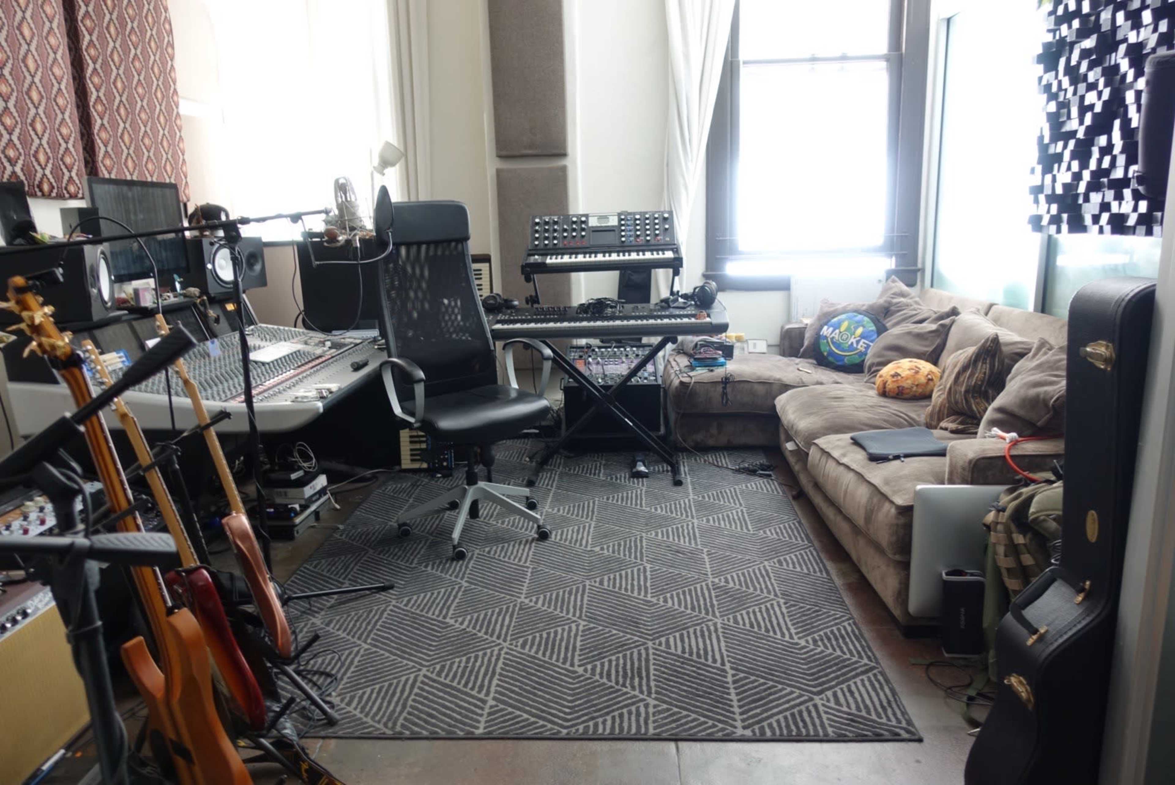 A music studio with a mixing console, various musical instruments, and a cozy sofa arranged around a patterned rug.