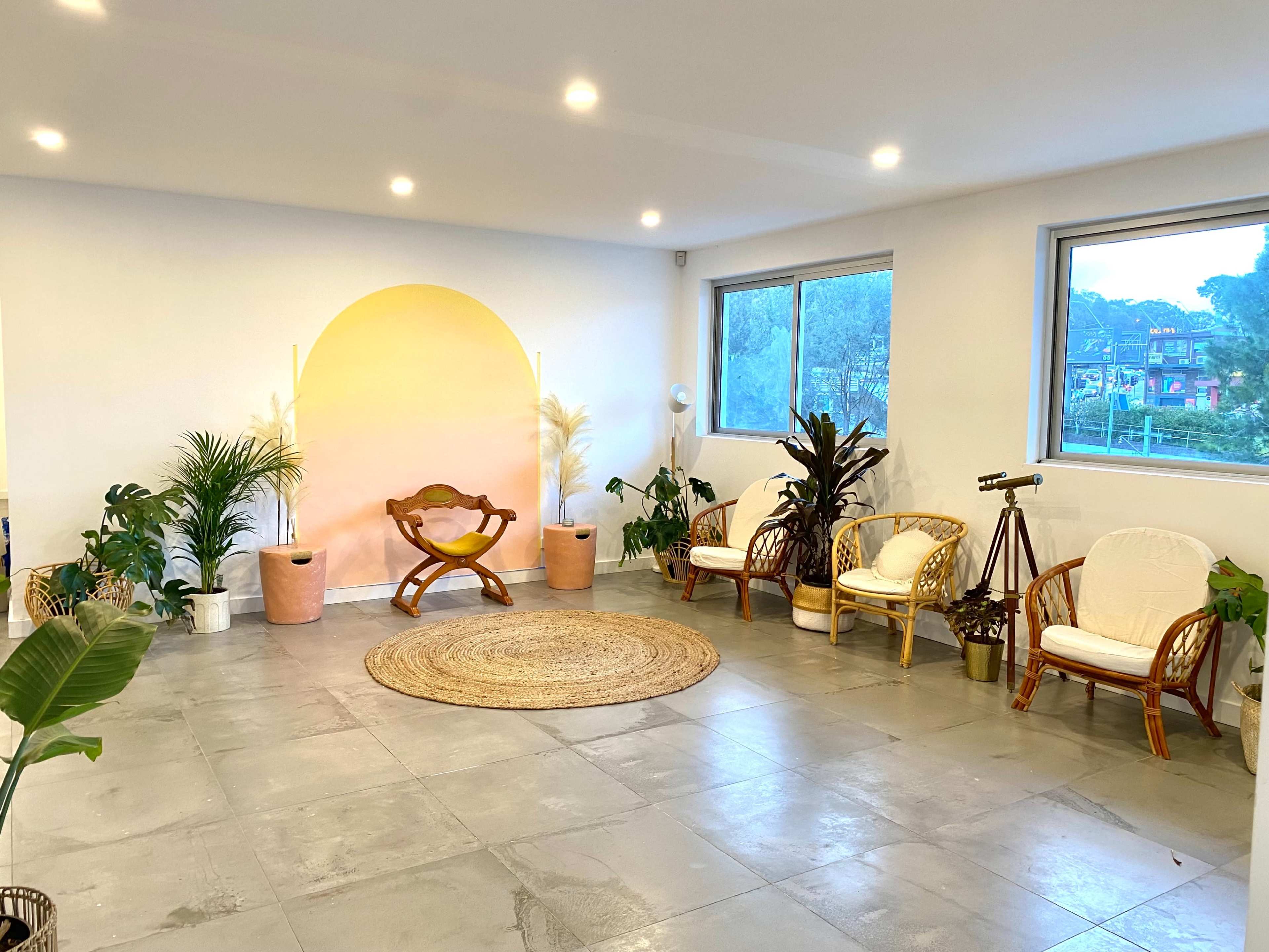 A spacious room features a light-colored wall with a circular mural, surrounded by various plants and seating arrangements.