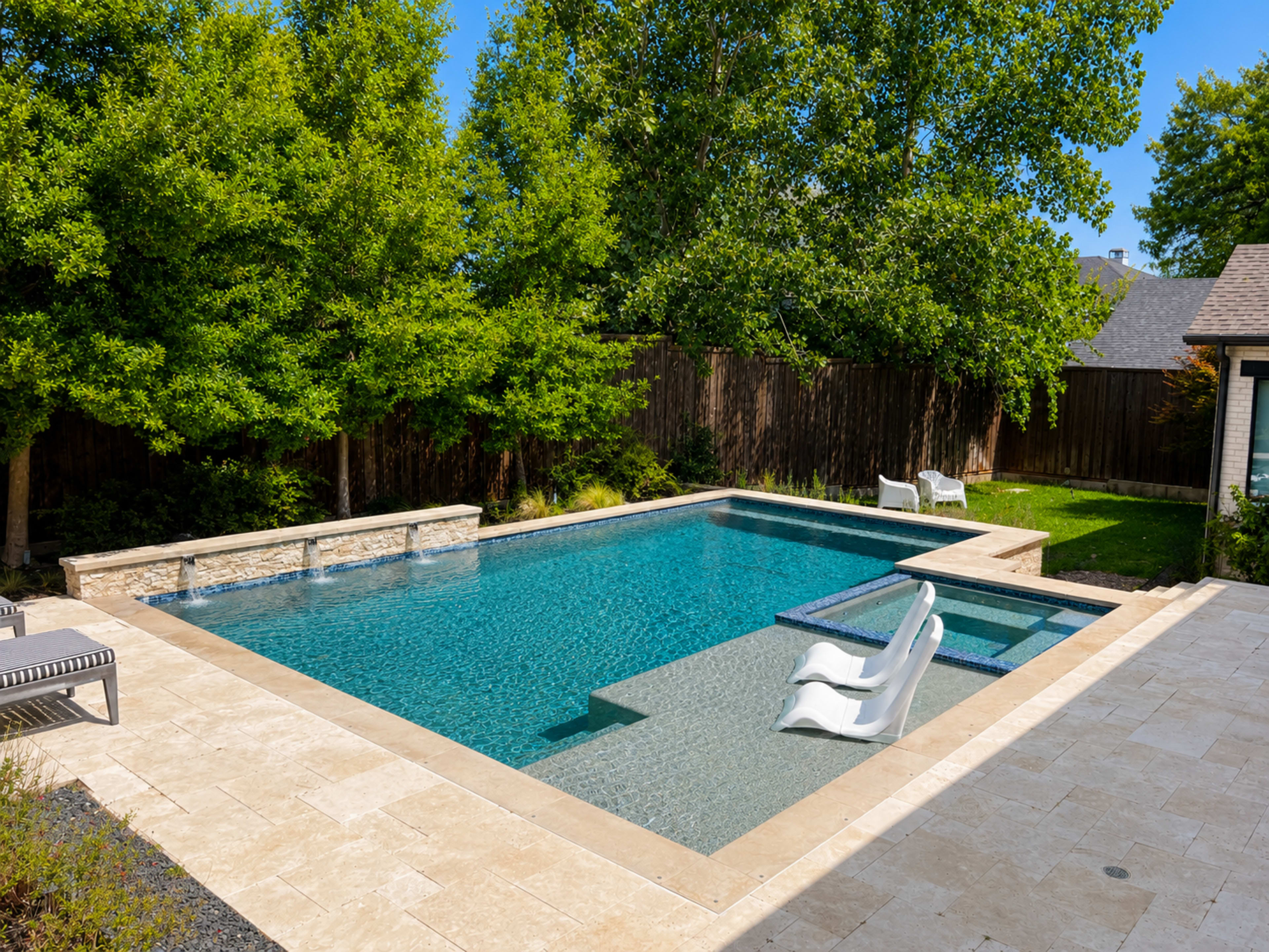 The image shows a modern swimming pool surrounded by stone patios and landscaped greenery.