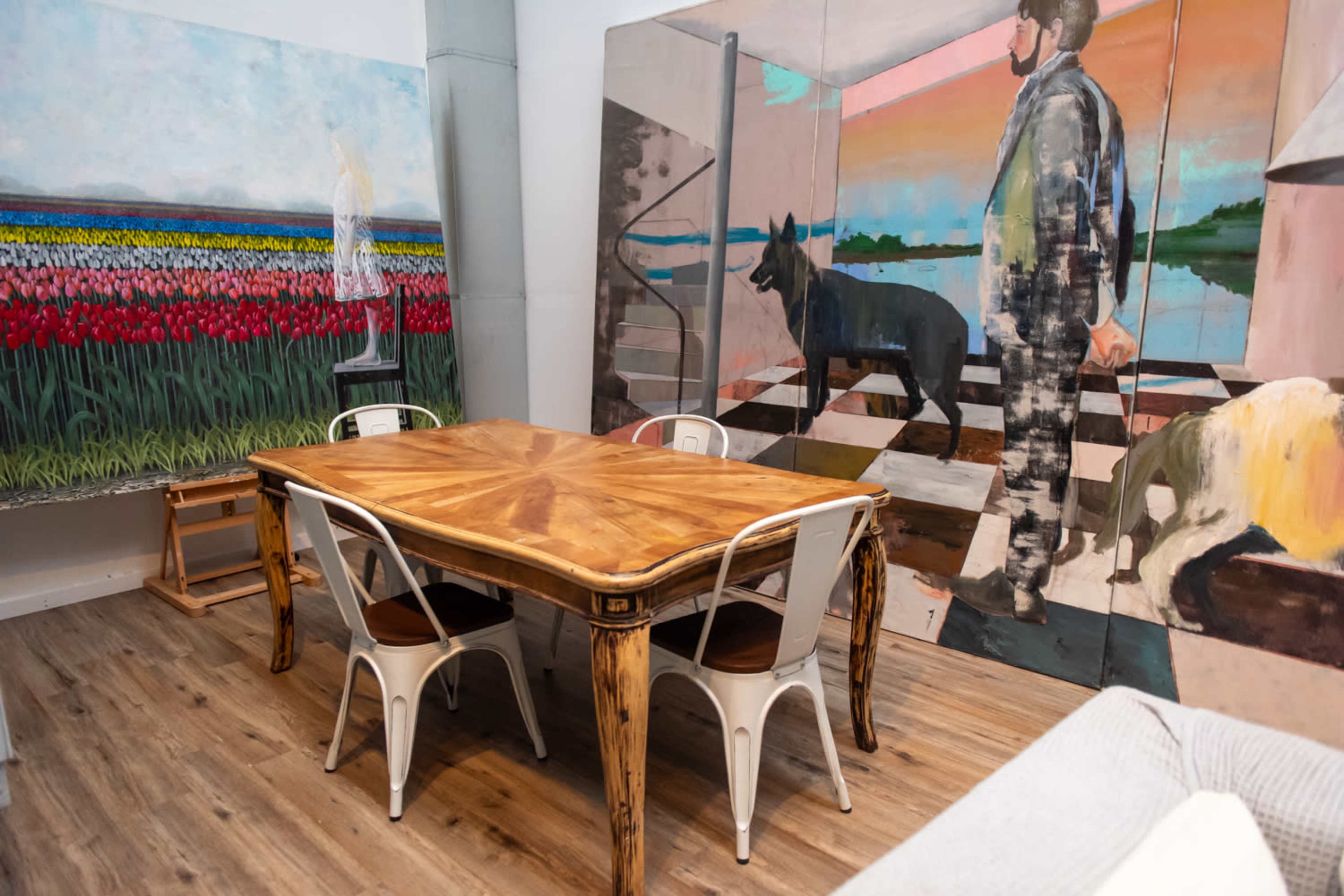 A wooden dining table surrounded by metal chairs in a room featuring large, colorful murals on the walls.