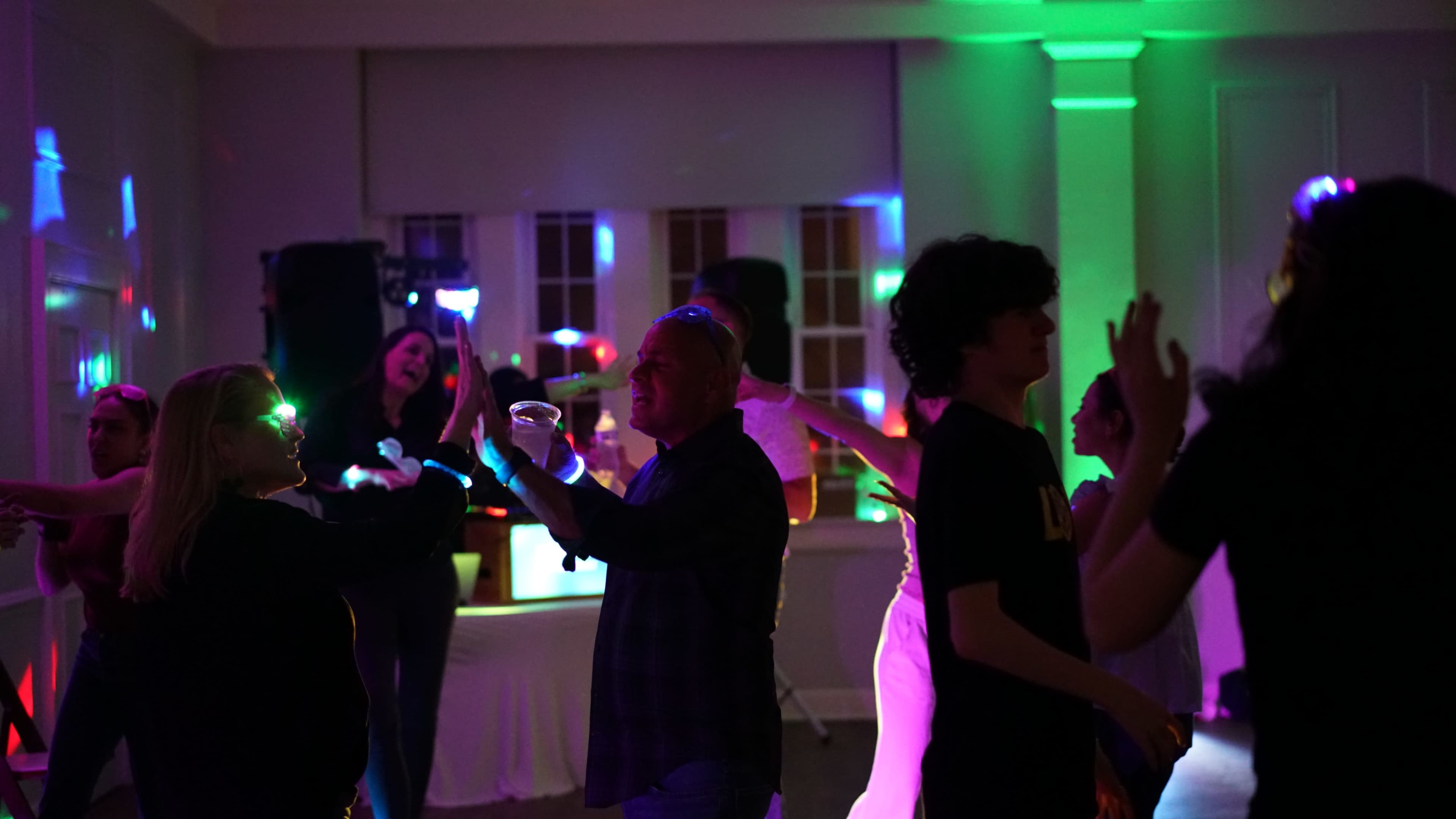 People dance in a brightly lit room with colored lights reflecting off the walls.