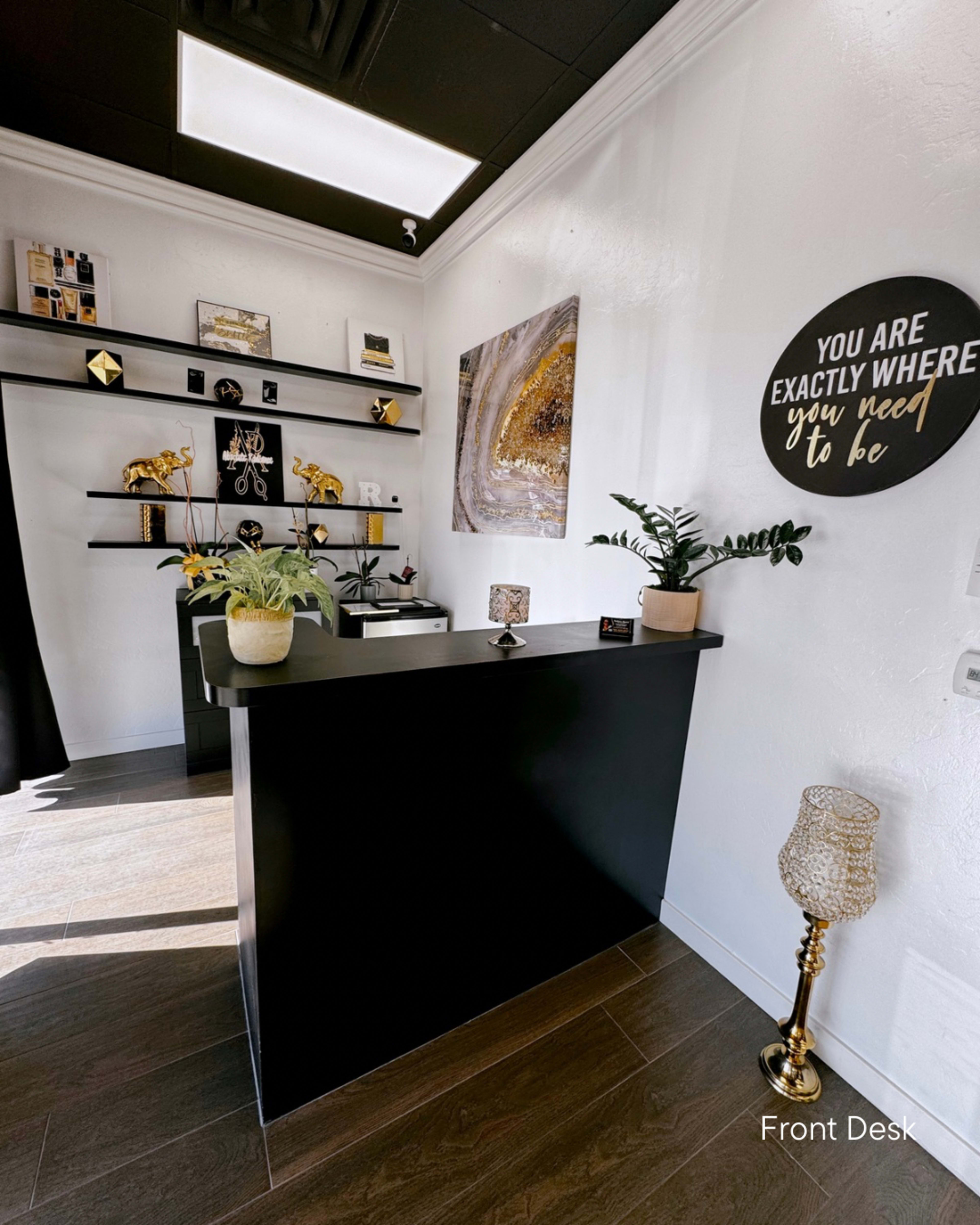 The image shows a modern reception area with a black front desk, decorative shelves, and plants.