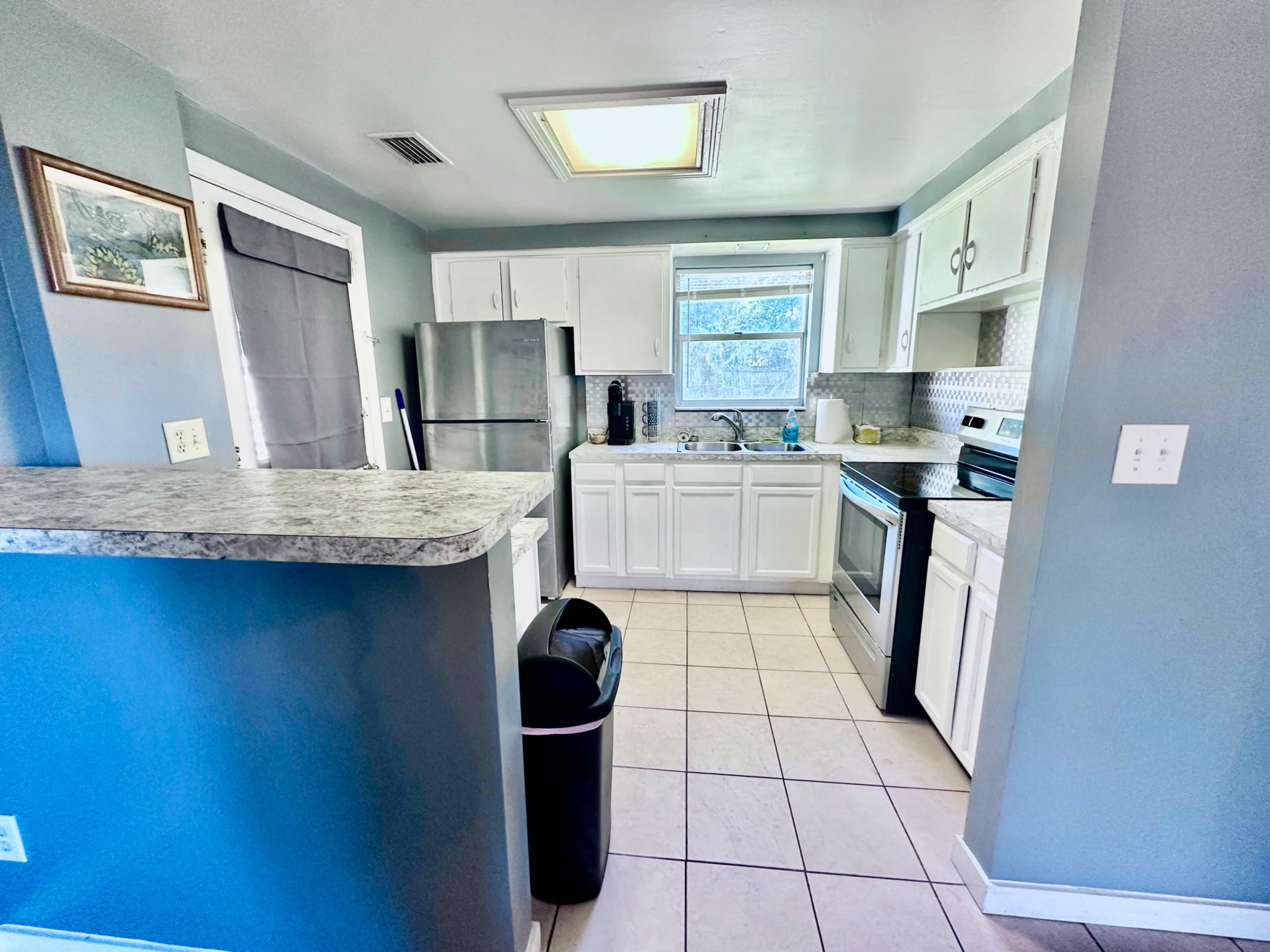 The image shows a modern kitchen with white cabinets, stainless steel appliances, and a tiled floor.
