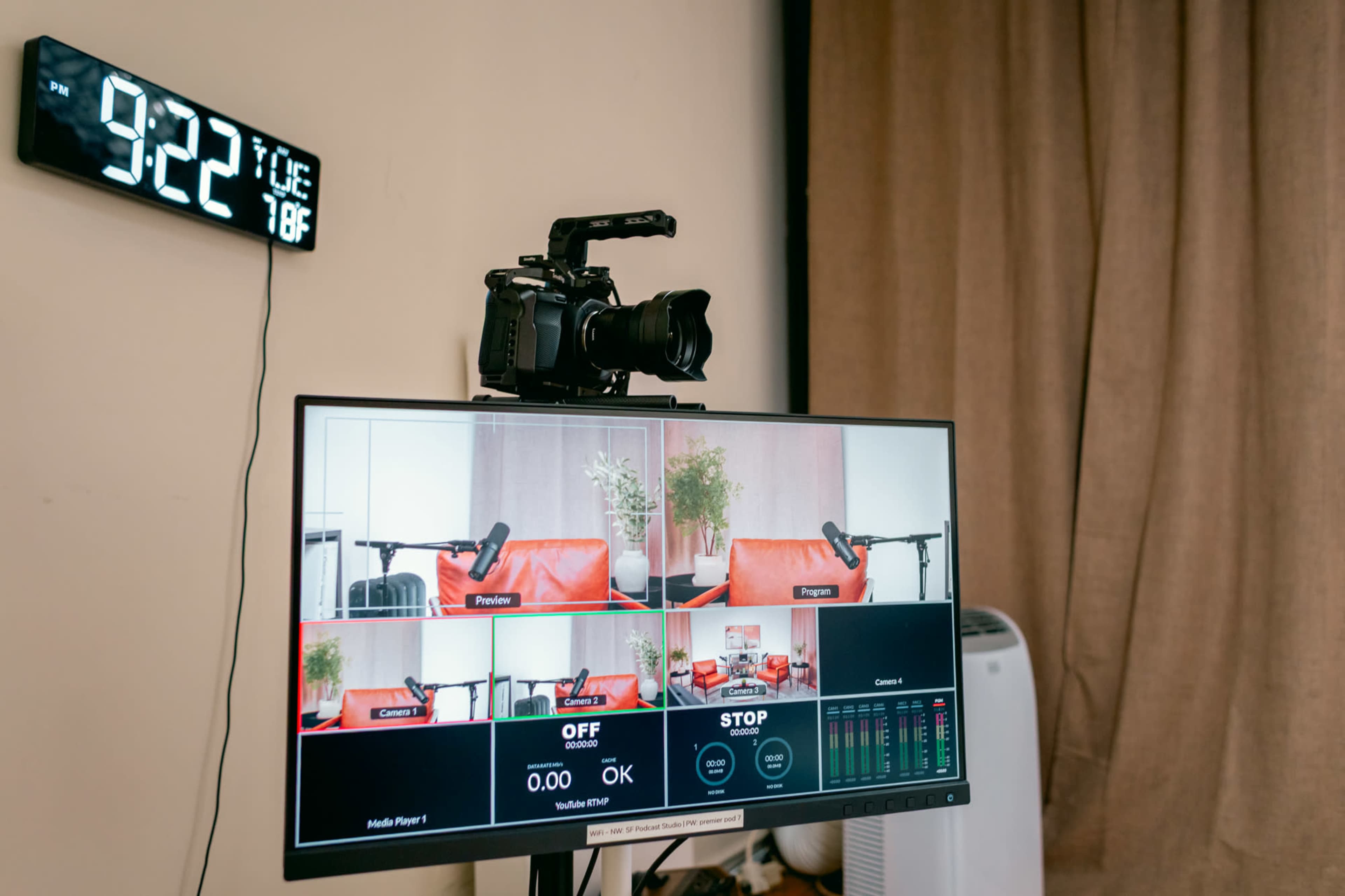A digital clock shows the time as 9:22, and a camera is positioned on top of a monitor displaying multiple camera feeds.