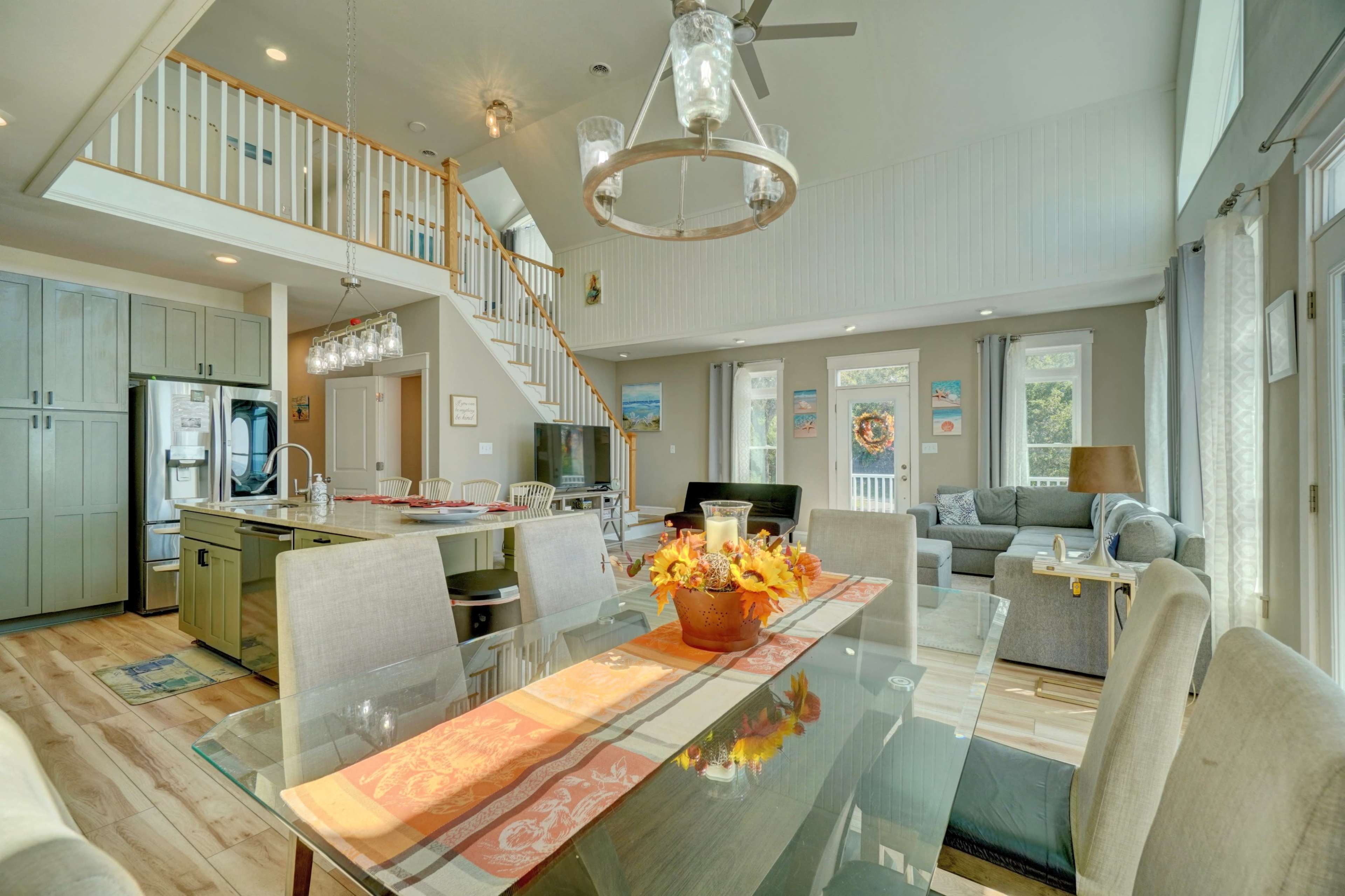 The image shows a modern open-concept living space featuring a kitchen, dining area, and living room with large windows and hardwood flooring.