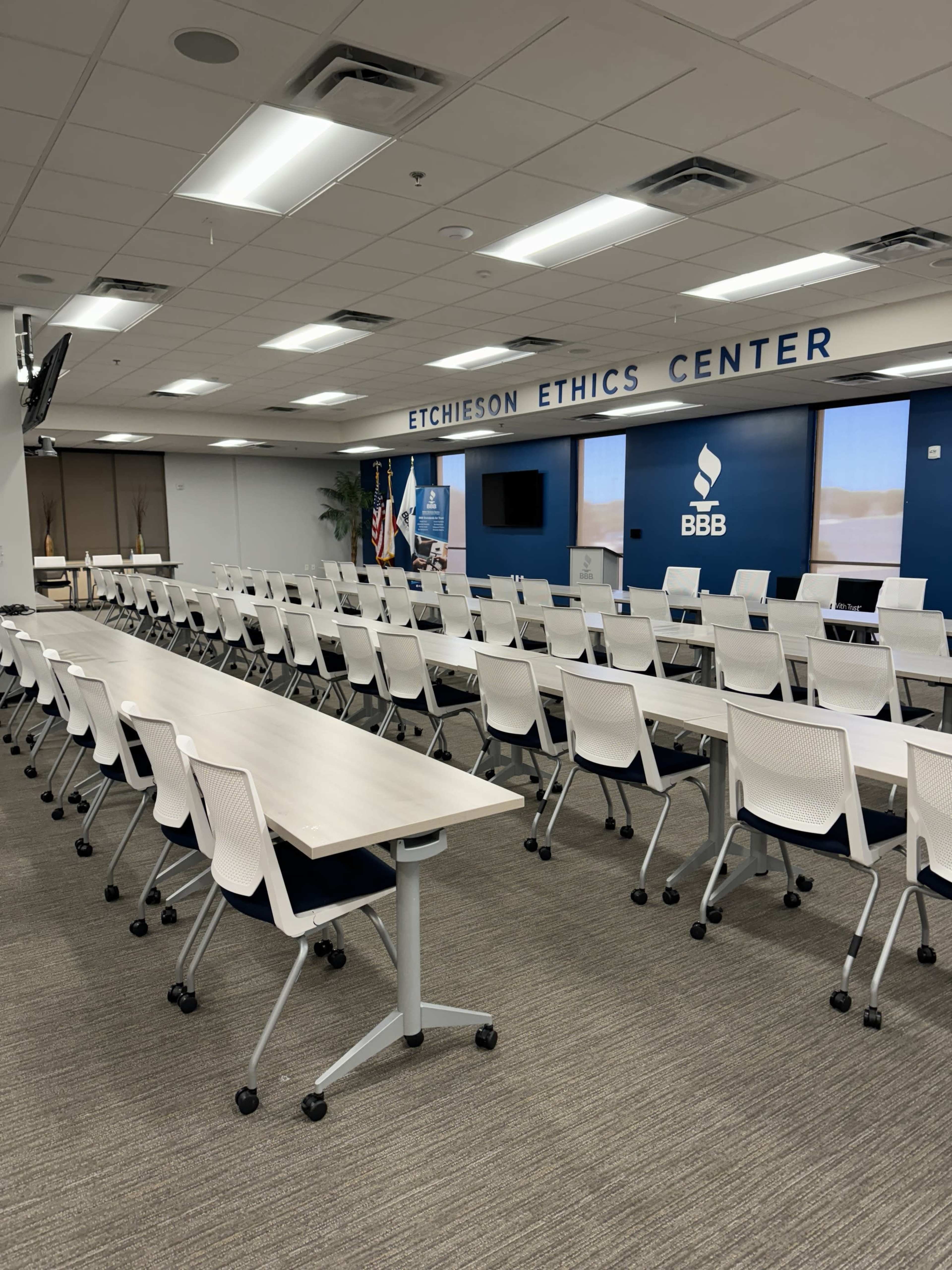A large conference room with rows of movable tables and chairs, featuring a wall displaying the "Etchieson Ethics Center" sign and a screen for presentations.