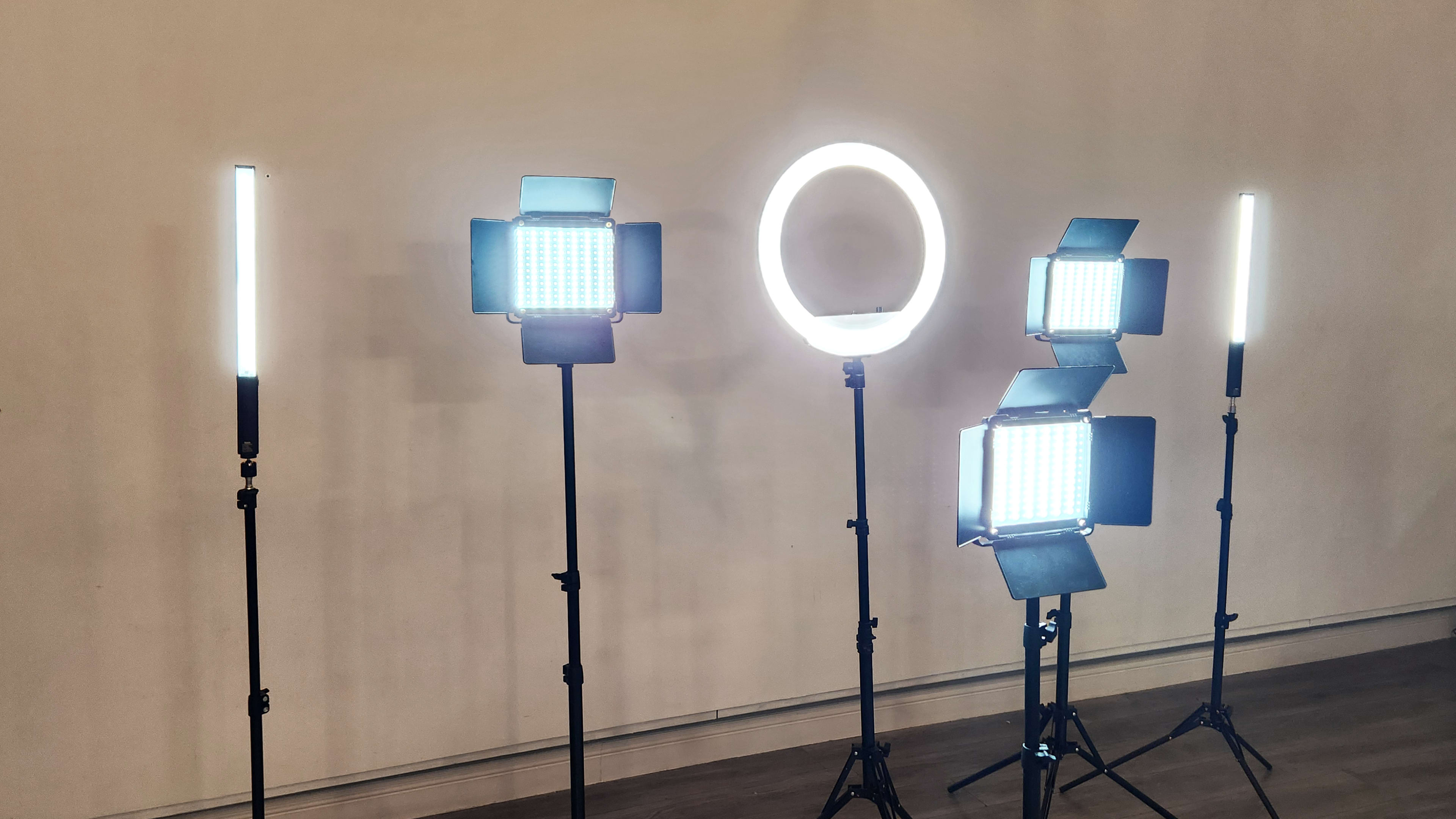 Various lighting equipment, including LED panels and a ring light, arranged on tripods in a studio setting.