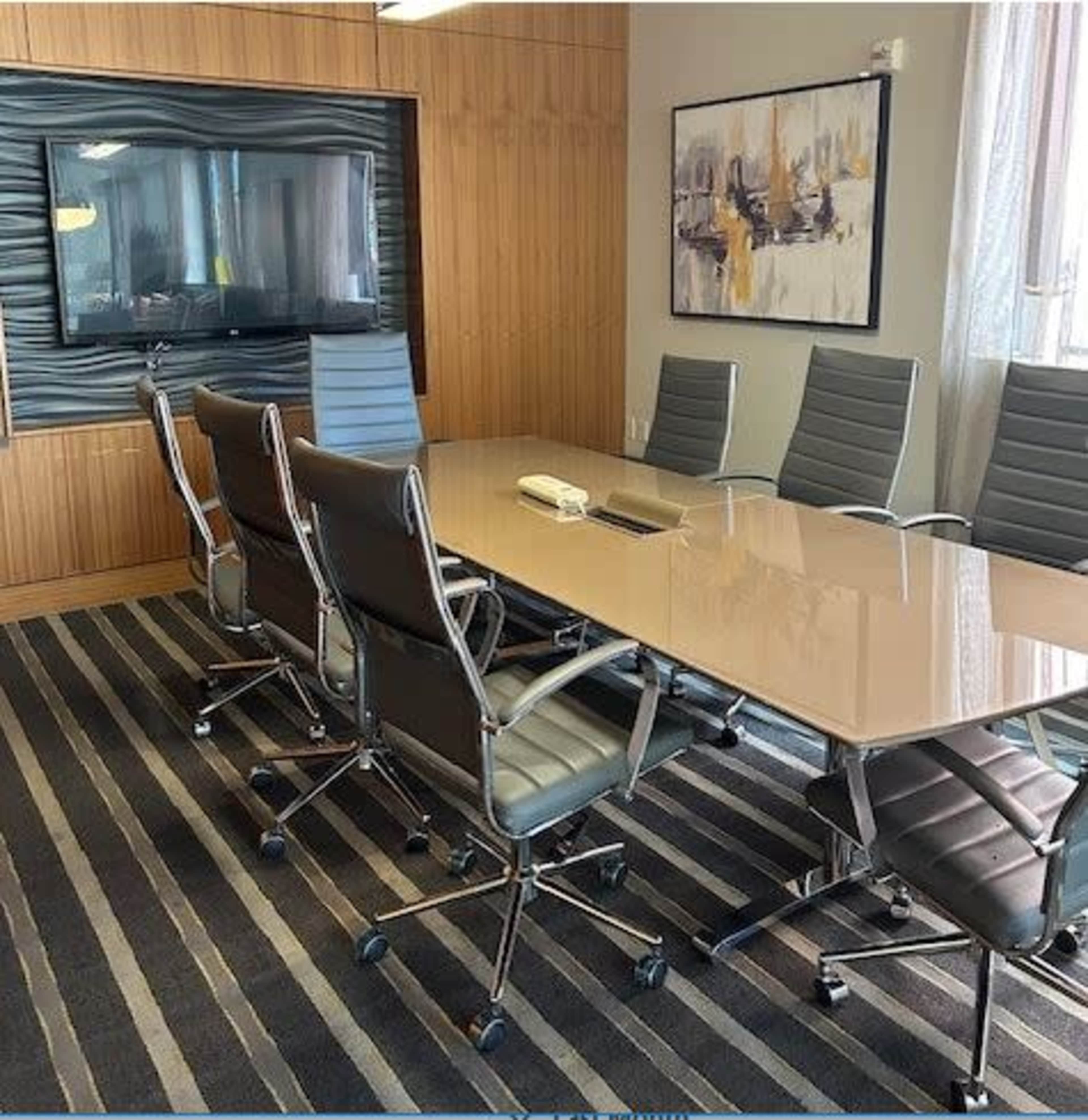 A modern conference room features a large glass table surrounded by ergonomic chairs, with a wall-mounted screen in the background.