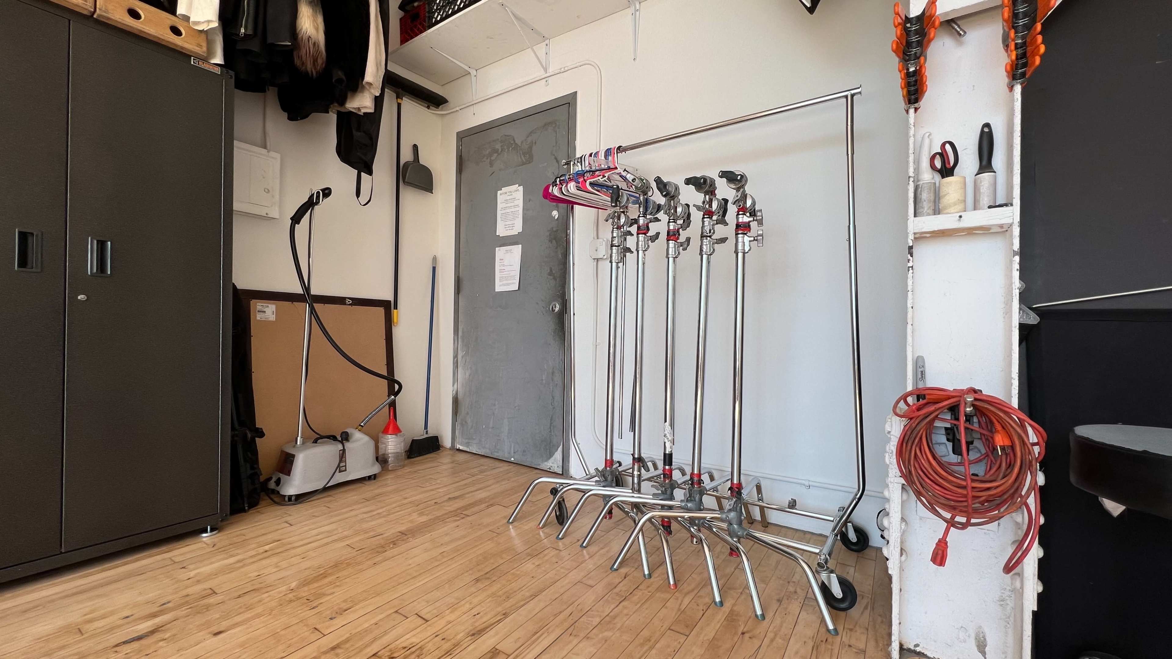 The image shows a well-organized room featuring a clothing rack with hangers, a vacuum cleaner, and various tools against a white wall.