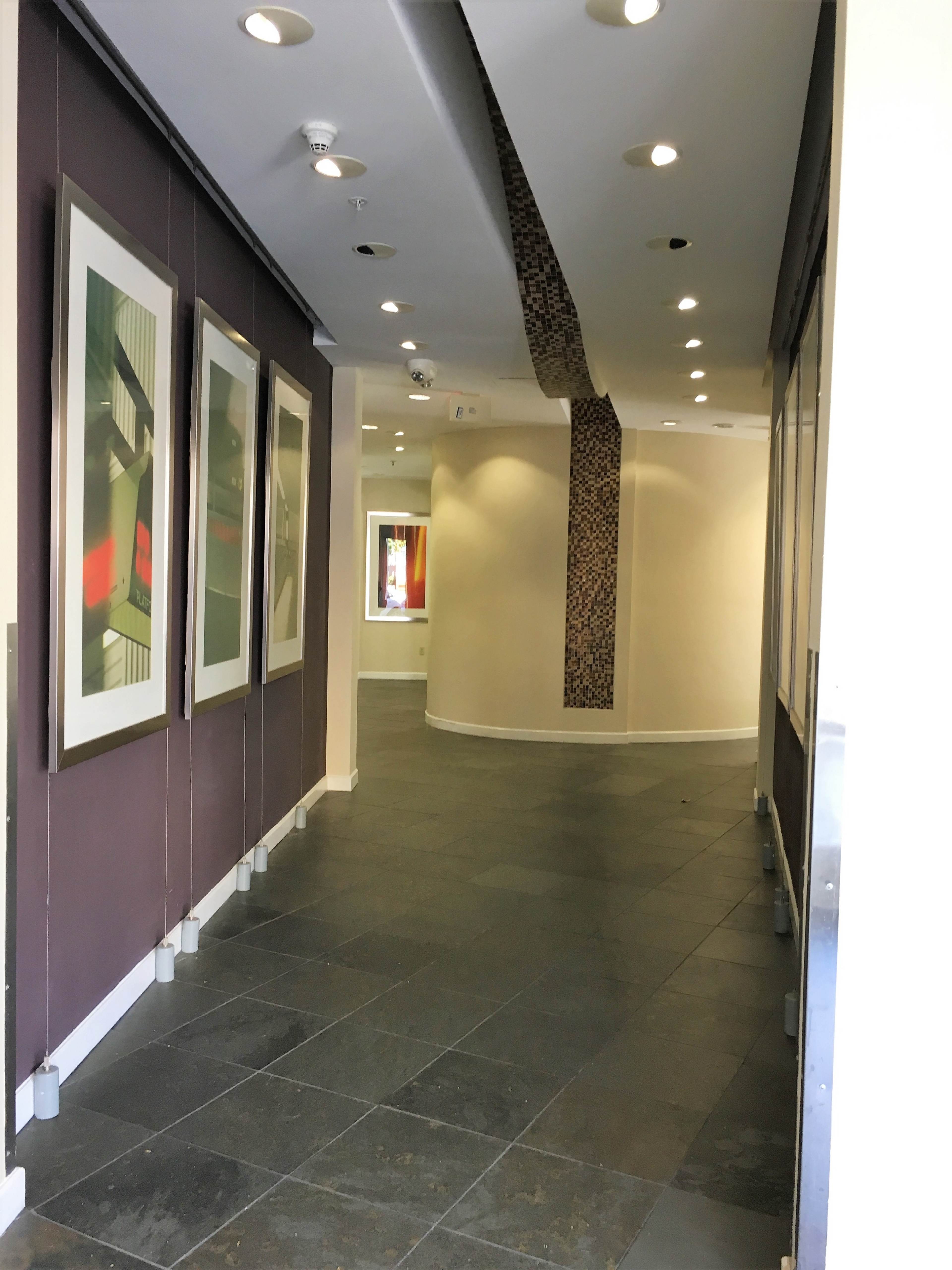 A corridor with framed artworks on the walls and a smooth, tiled floor leading to a lighted space at the end.