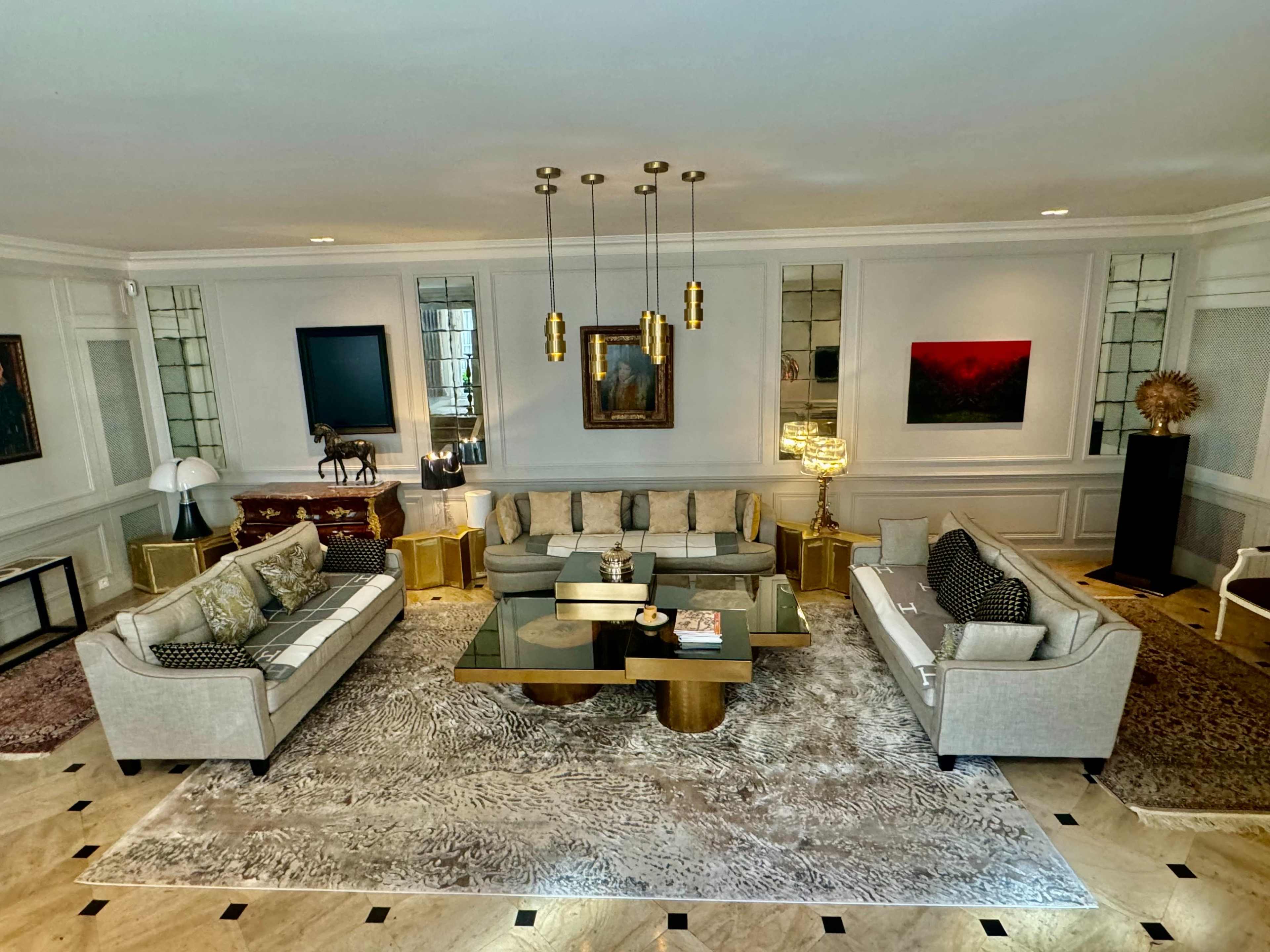 The living room features gray sofas arranged around a glass coffee table on a patterned rug, with decorative mirrors and a mix of modern and classic furniture.