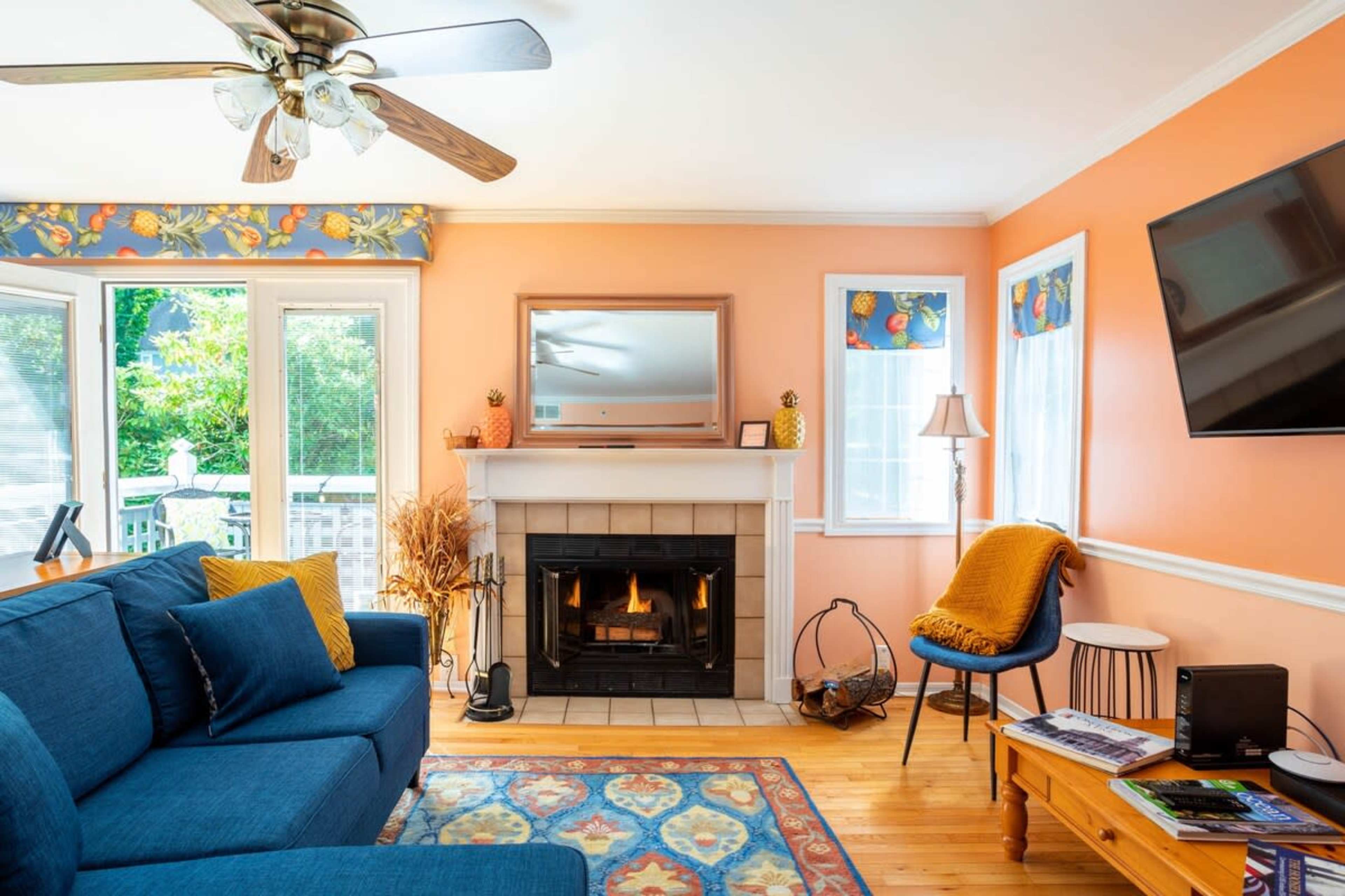 The living room features a blue sofa, a fireplace with a mantel, and large windows surrounded by orange walls.