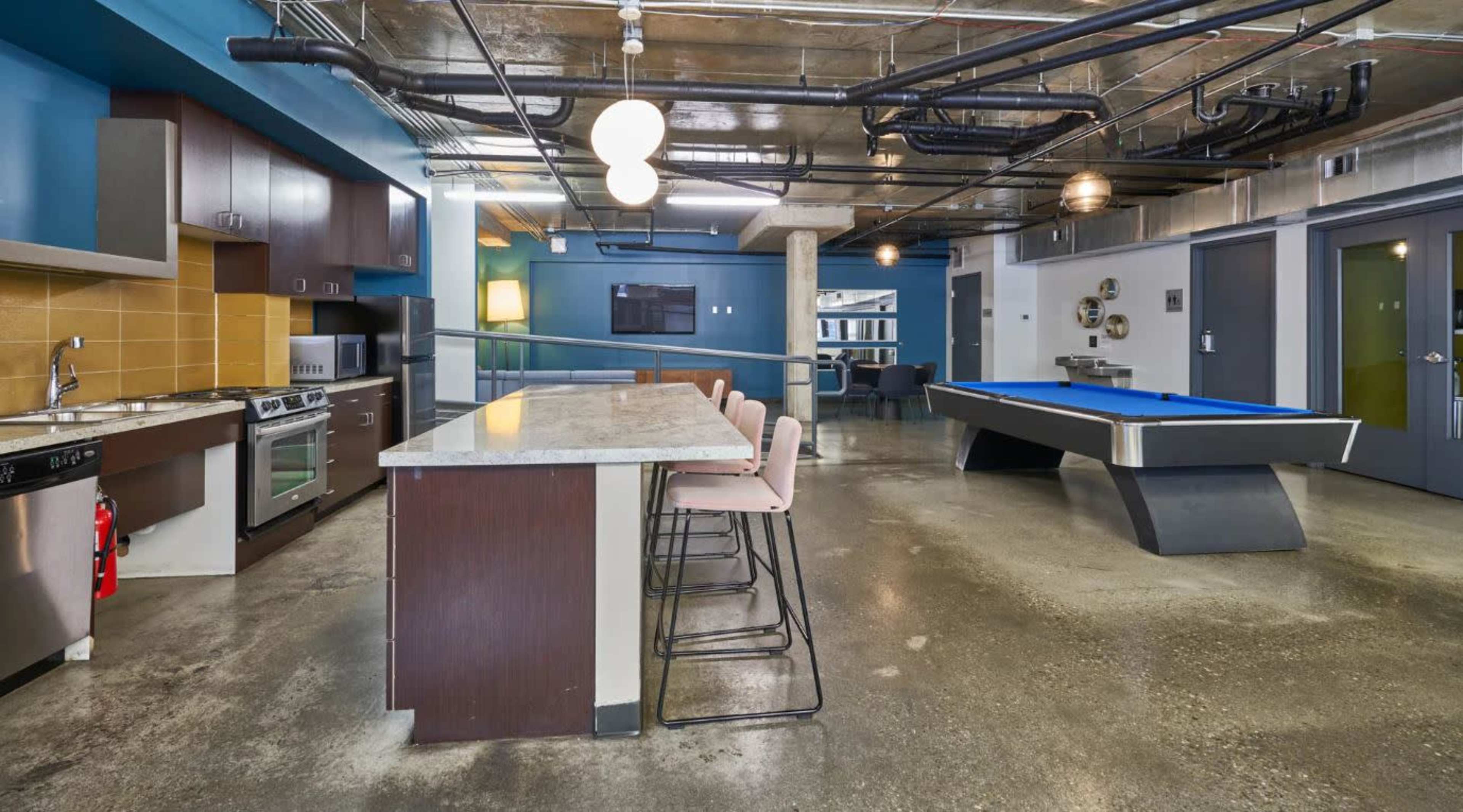 The image shows a modern open-concept kitchen and recreational area featuring a kitchen island with seating, a pool table, and industrial-style decor.
