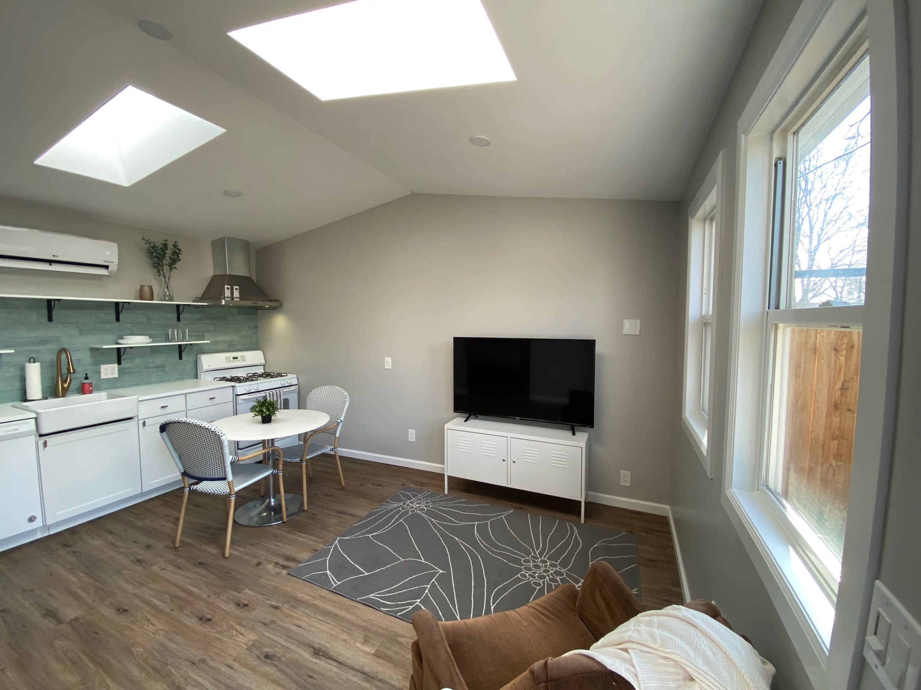 The image shows a modern, open-concept living area with a kitchen, dining table, and a television.