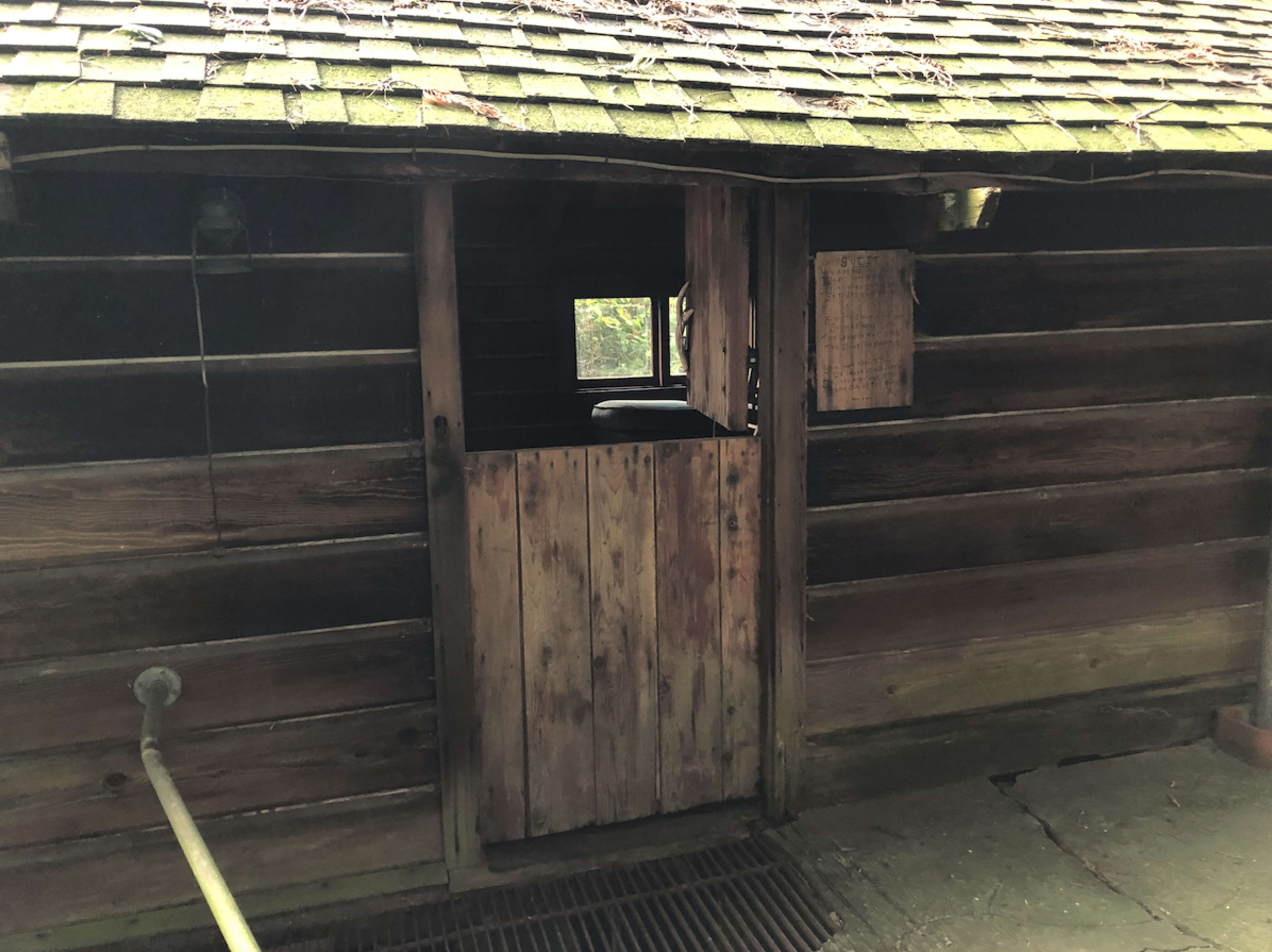 A rustic wooden cabin features a partially open door and a small window.