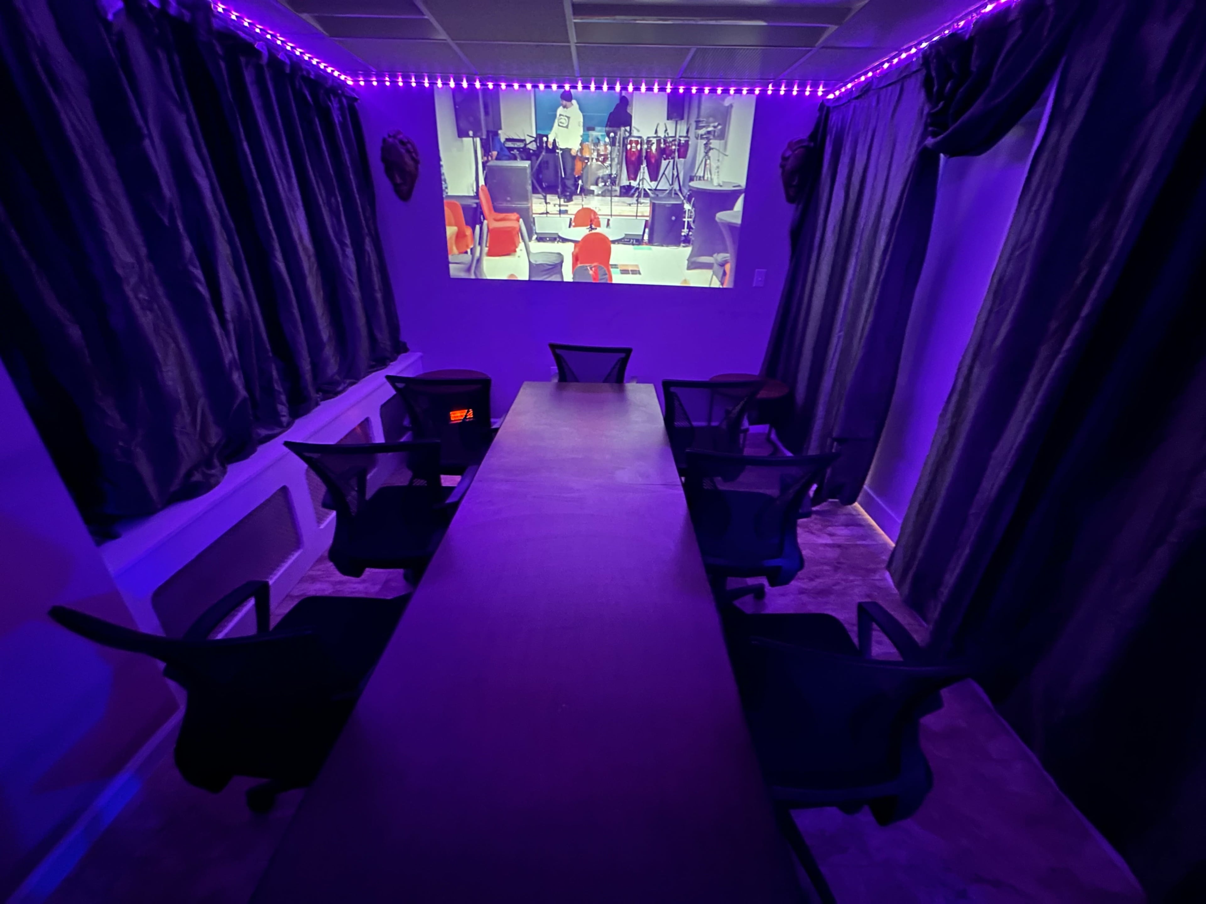 A dimly lit conference room features a long table surrounded by chairs, with a projected screen displaying a colorful animated scene.