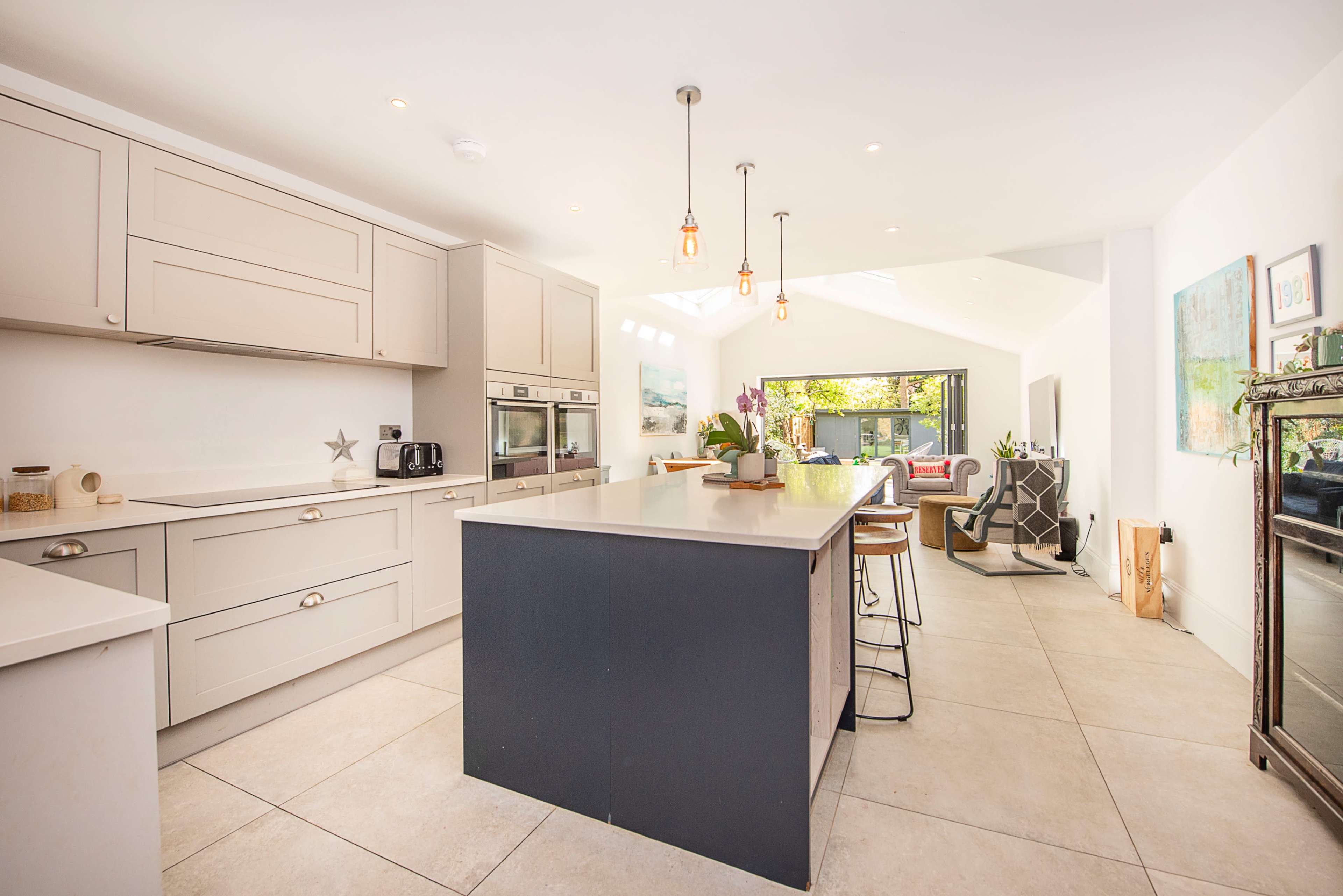 The image shows a modern kitchen with light-colored cabinetry, a central island, and large windows that provide natural light.