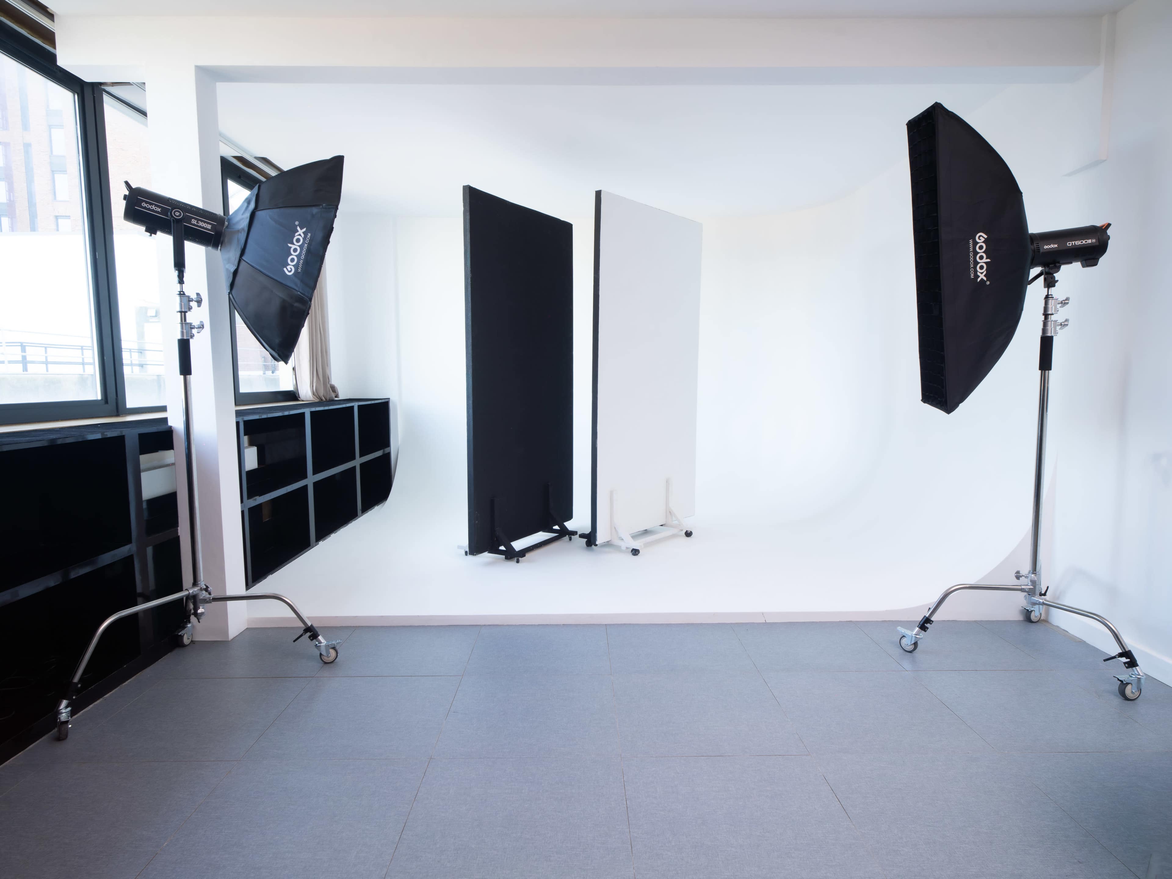 The image shows a photography studio with two large softboxes and a seamless backdrop in black and white.