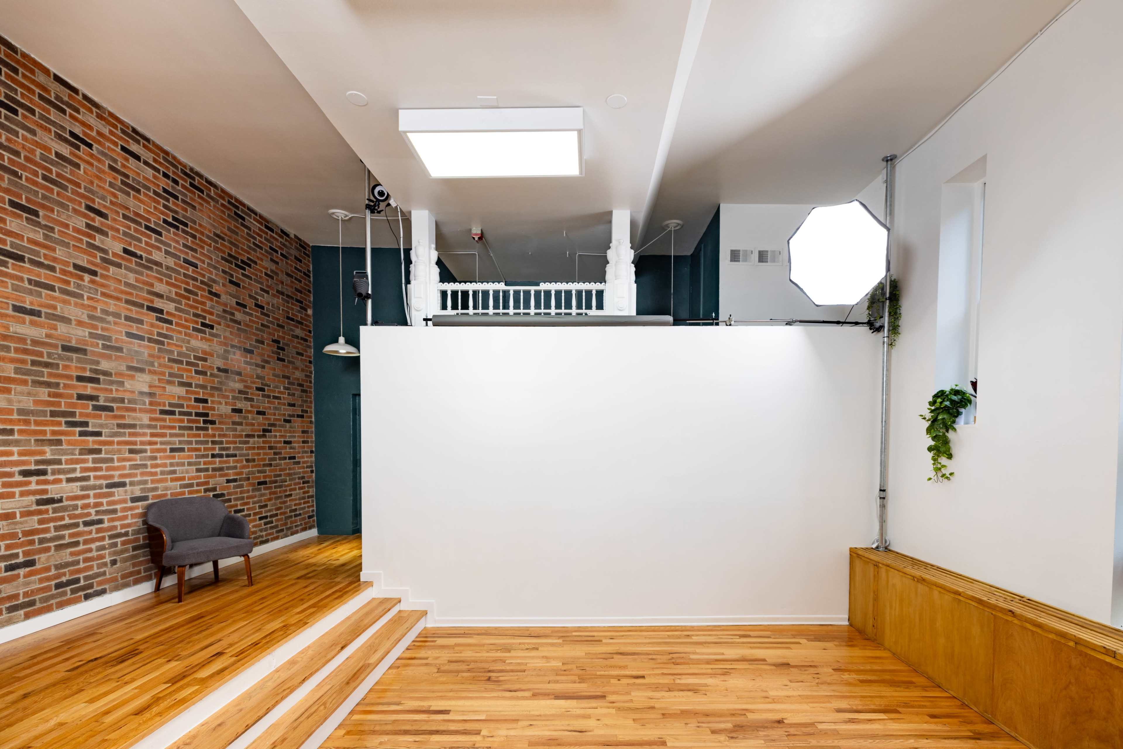 The interior space features a brick wall, wooden flooring, a staircase leading to a mezzanine, and large windows providing natural light.