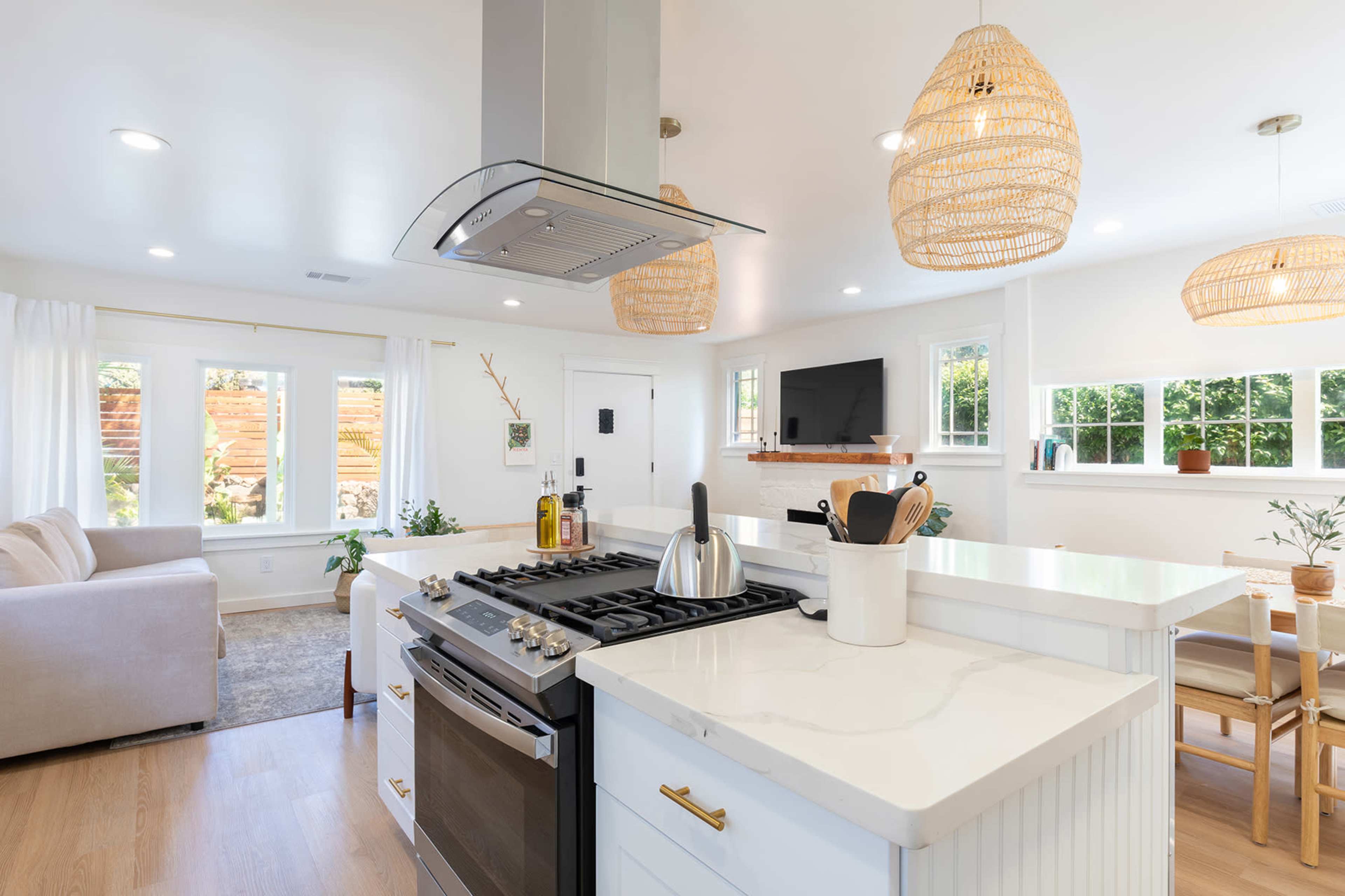 A modern kitchen features a gas stove, white cabinetry, and woven pendant lights, with open access to a bright living area.