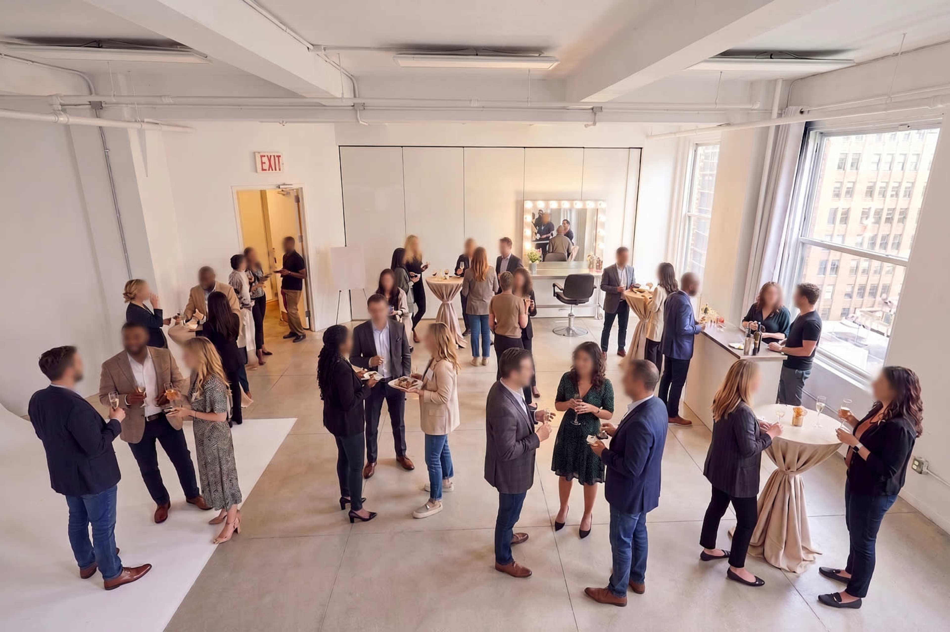 A group of people socialize at a networking event in a well-lit, spacious room with modern decor and tall windows.