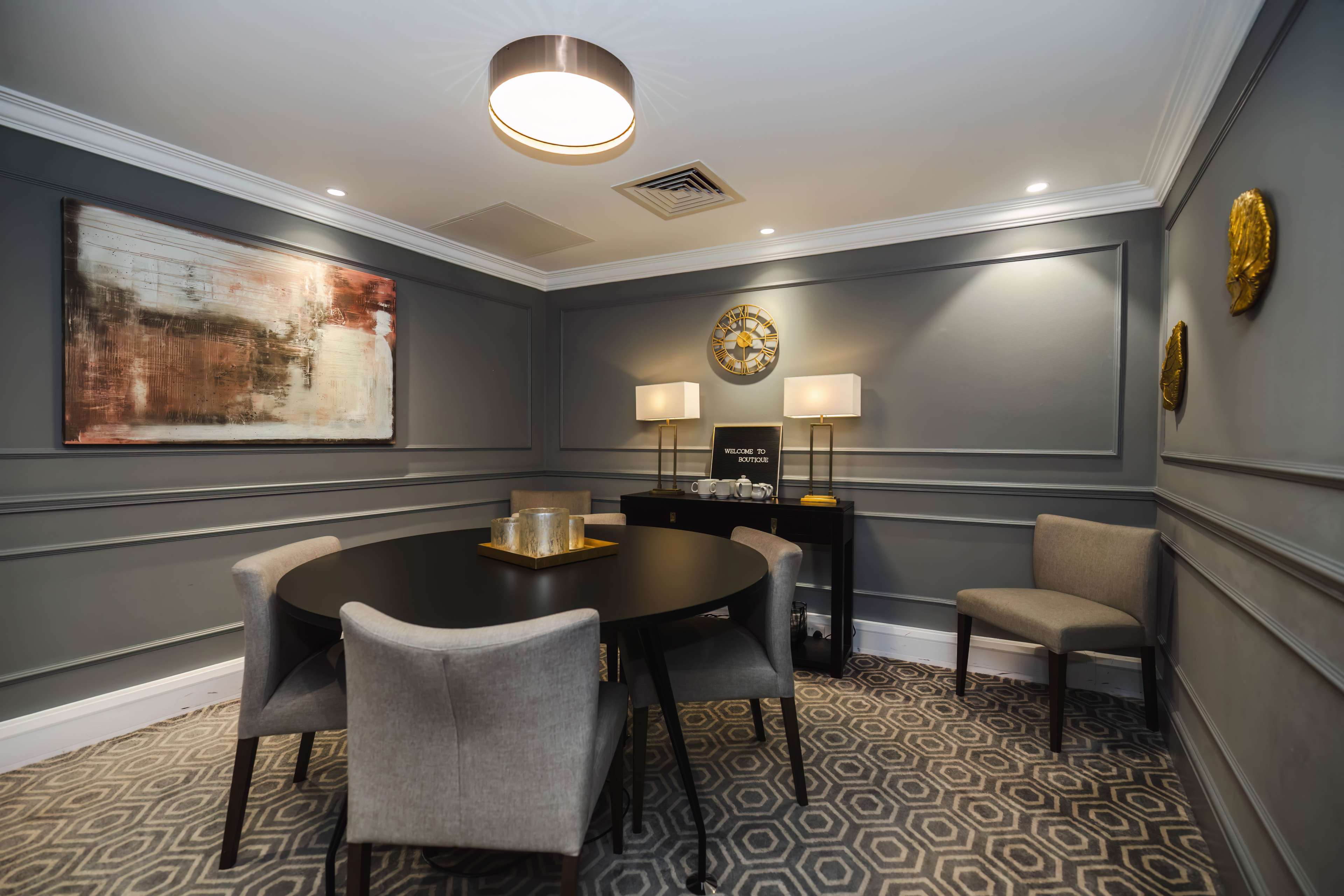 A small meeting room with a round black table, four chairs, a sideboard, and decorative wall art.