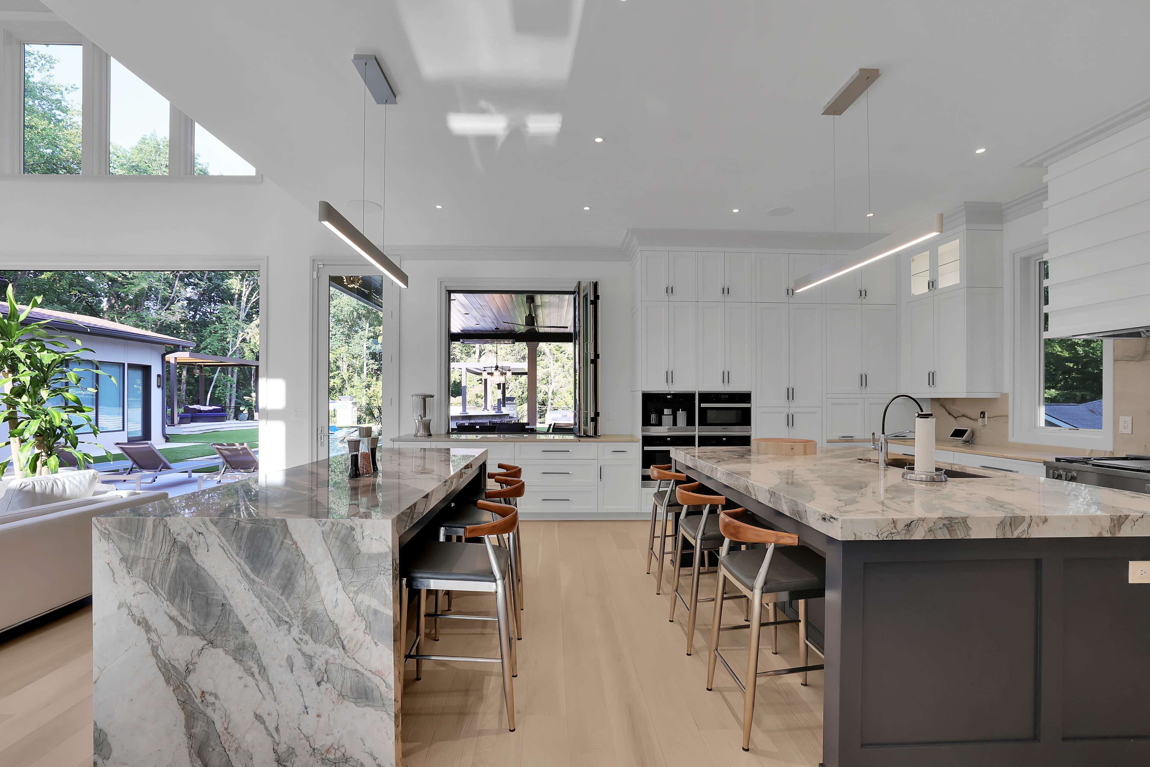 The kitchen features a large island with a marble countertop, white cabinetry, and modern lighting, overlooking an outdoor space with a pool.