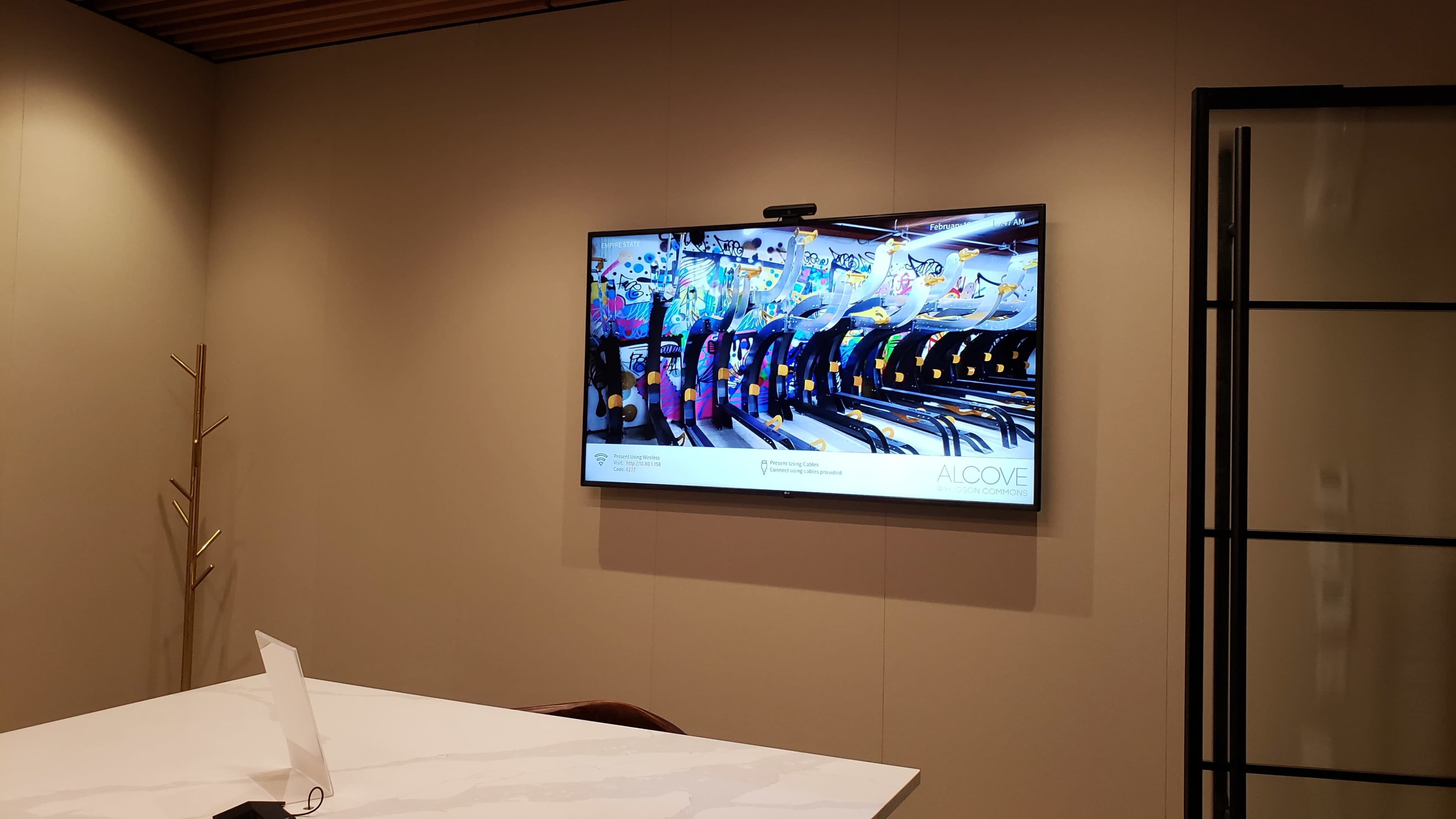 A large television displaying colorful graphics and images is mounted on a wall in a modern meeting room.