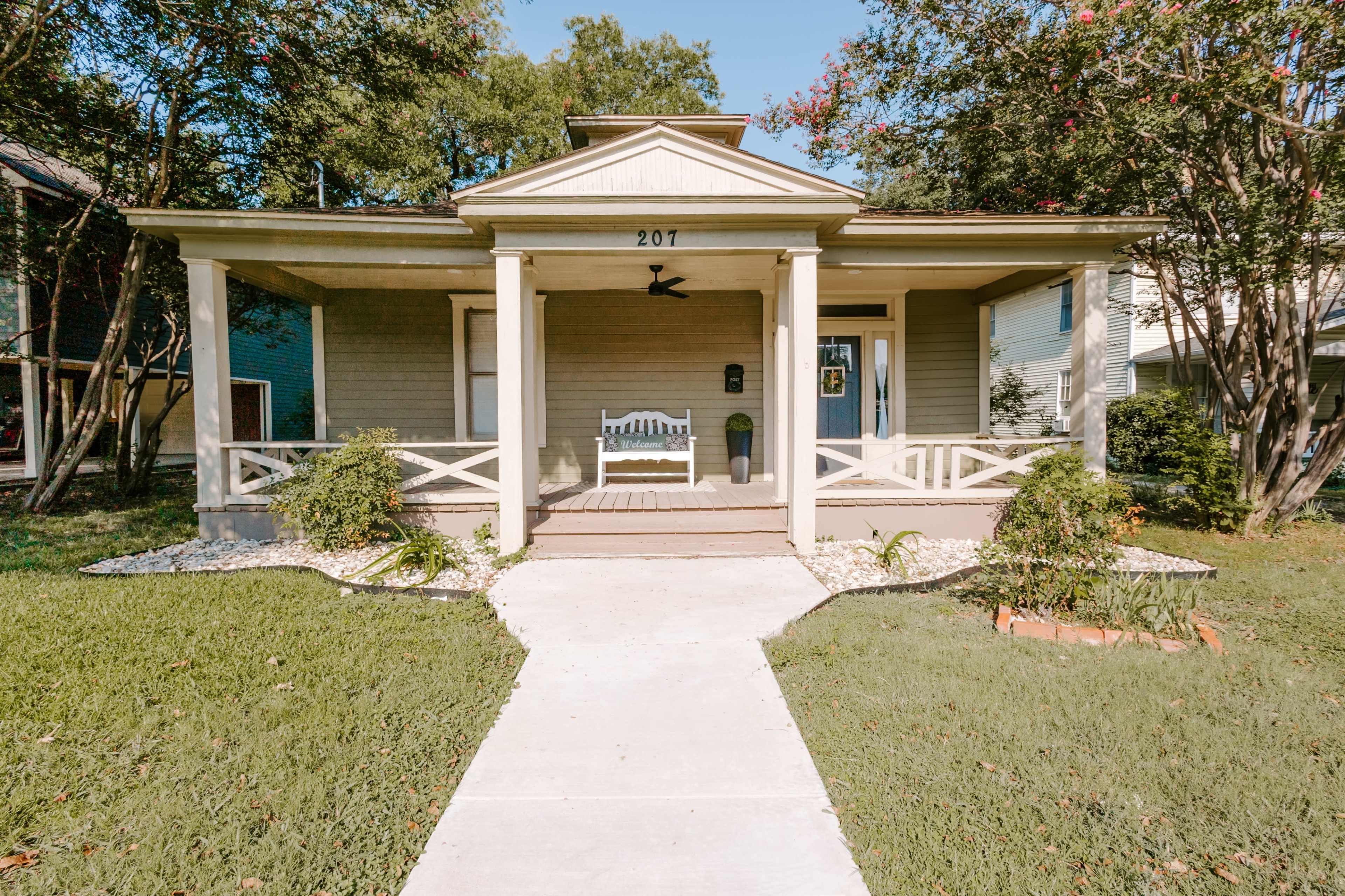 The image shows a front porch of a single-story house with a white bench and a walkway leading up to the entrance.