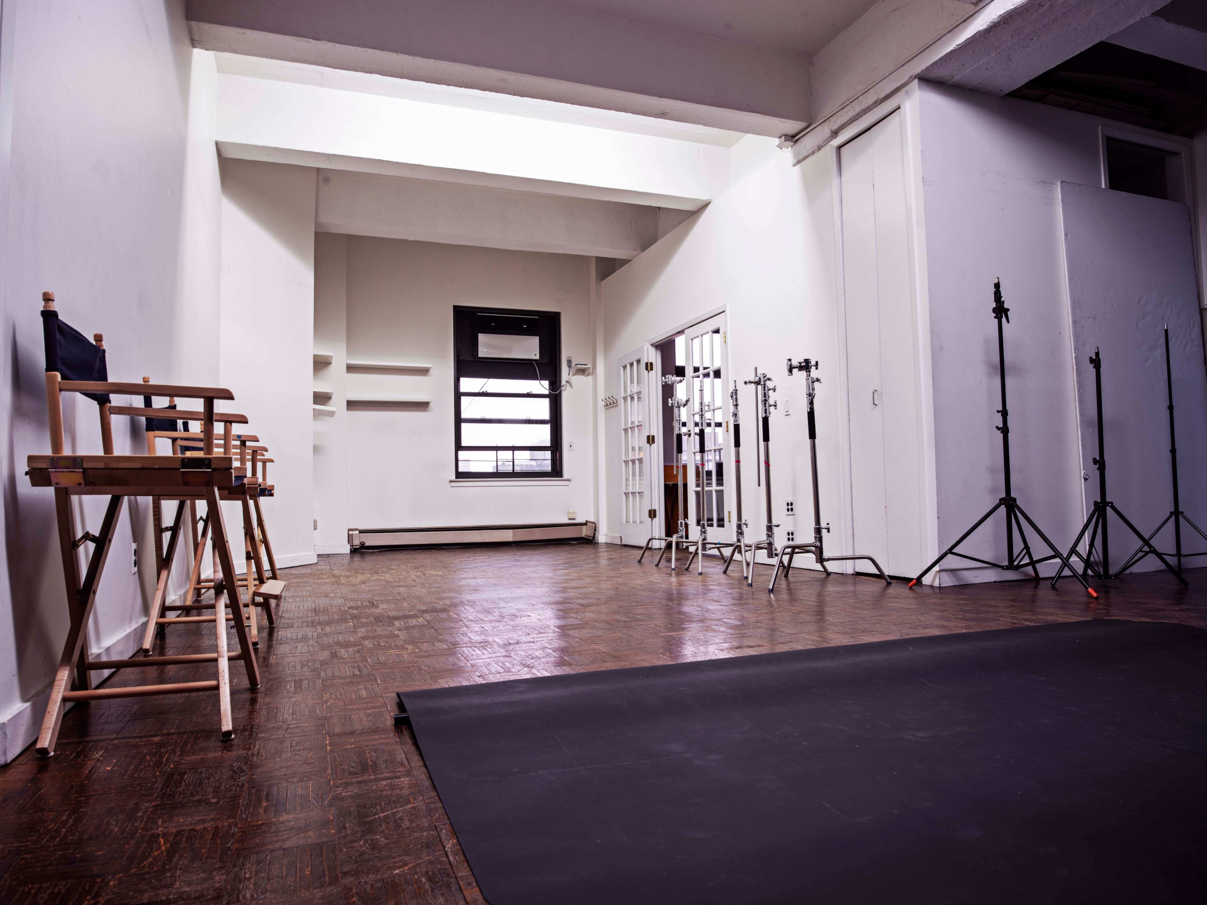 A spacious, empty studio with wooden flooring, equipped with director's chairs and lighting stands.