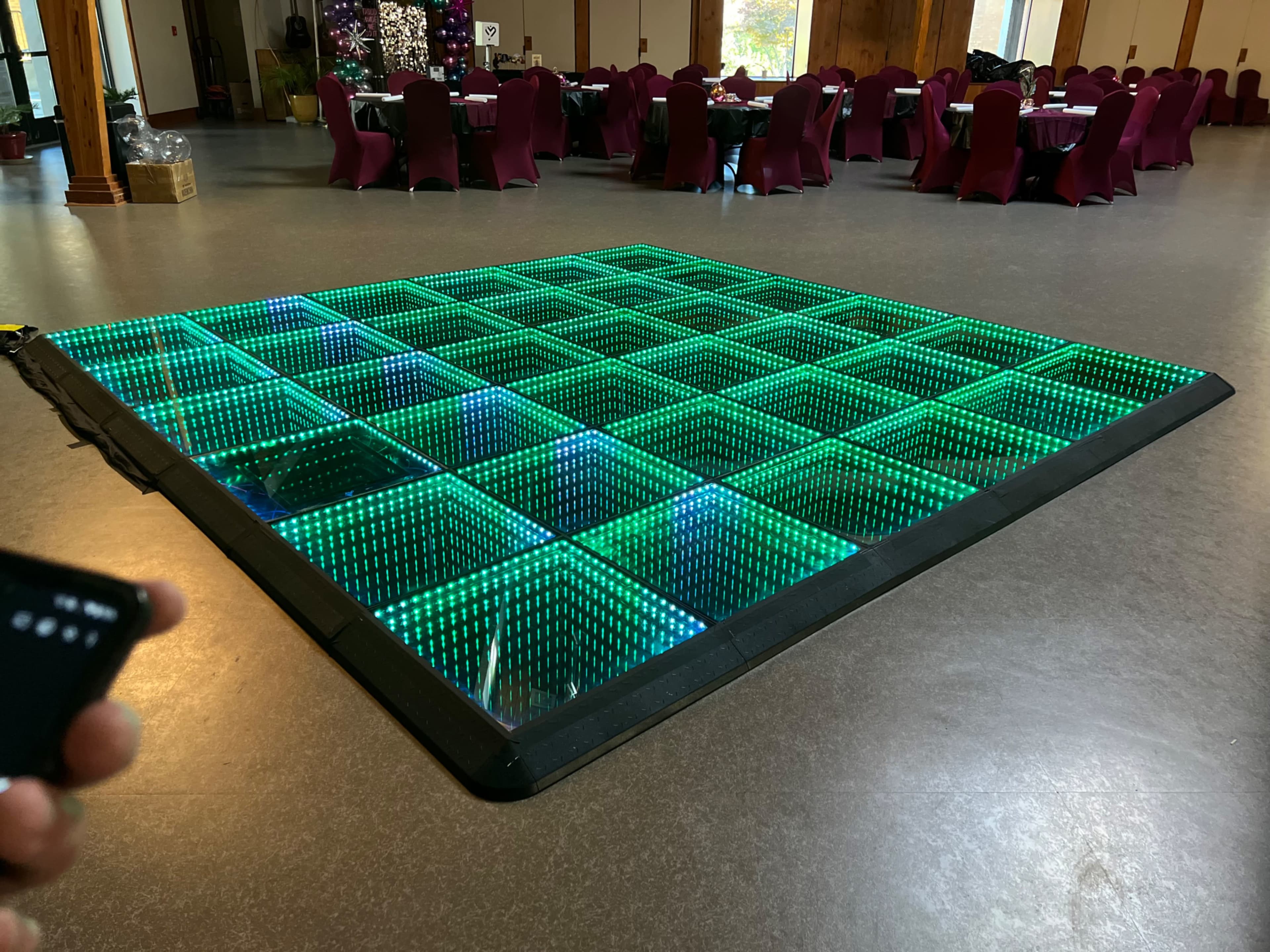 The image shows a large illuminated dance floor with a grid pattern, surrounded by tables covered in burgundy tablecloths.