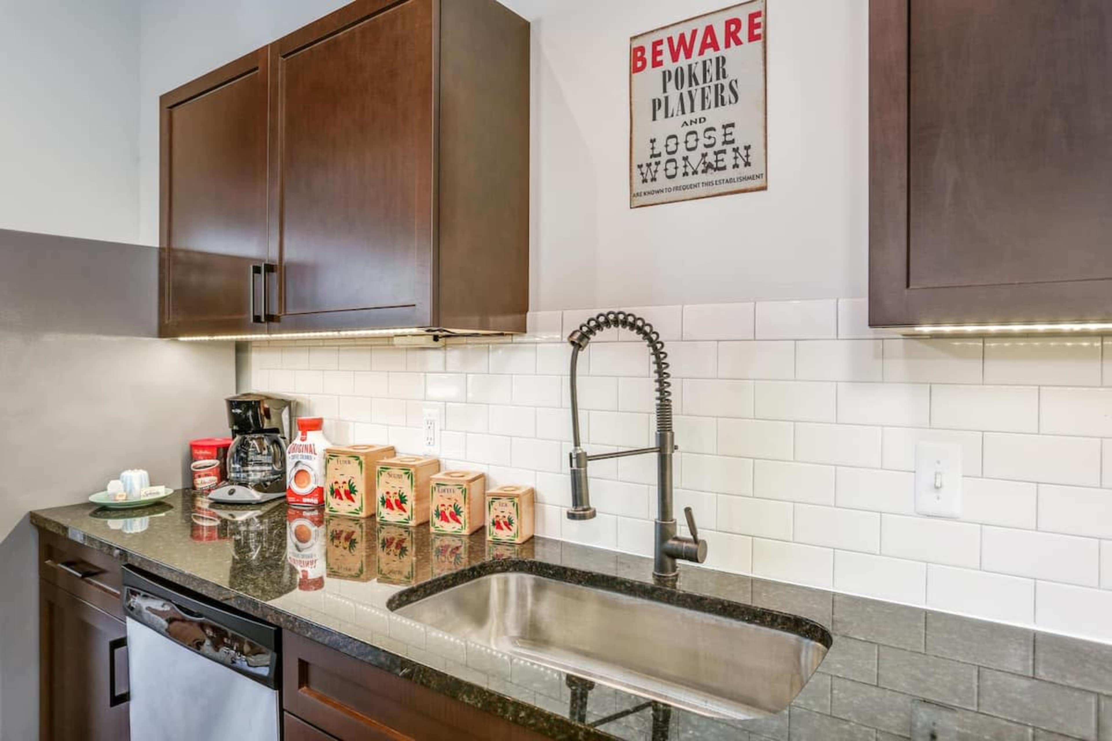 A kitchen features dark wooden cabinets, a stainless steel sink with a pull-down faucet, and a coffee maker, along with several decorative items on the counter.