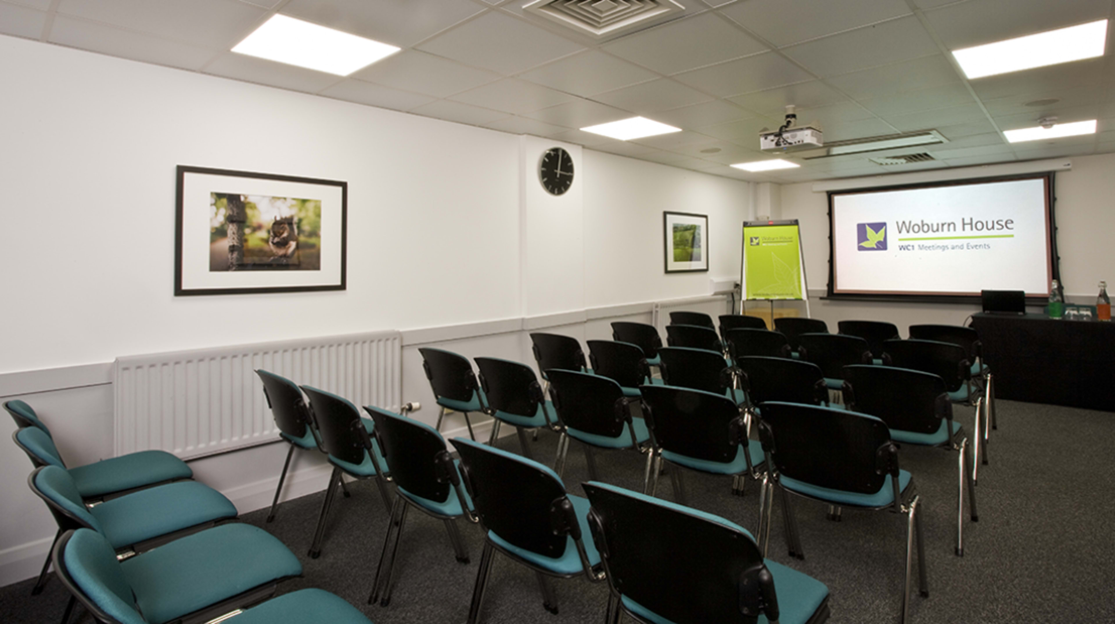 A conference room is set up with rows of chairs facing a projection screen and a presentation area at the front.