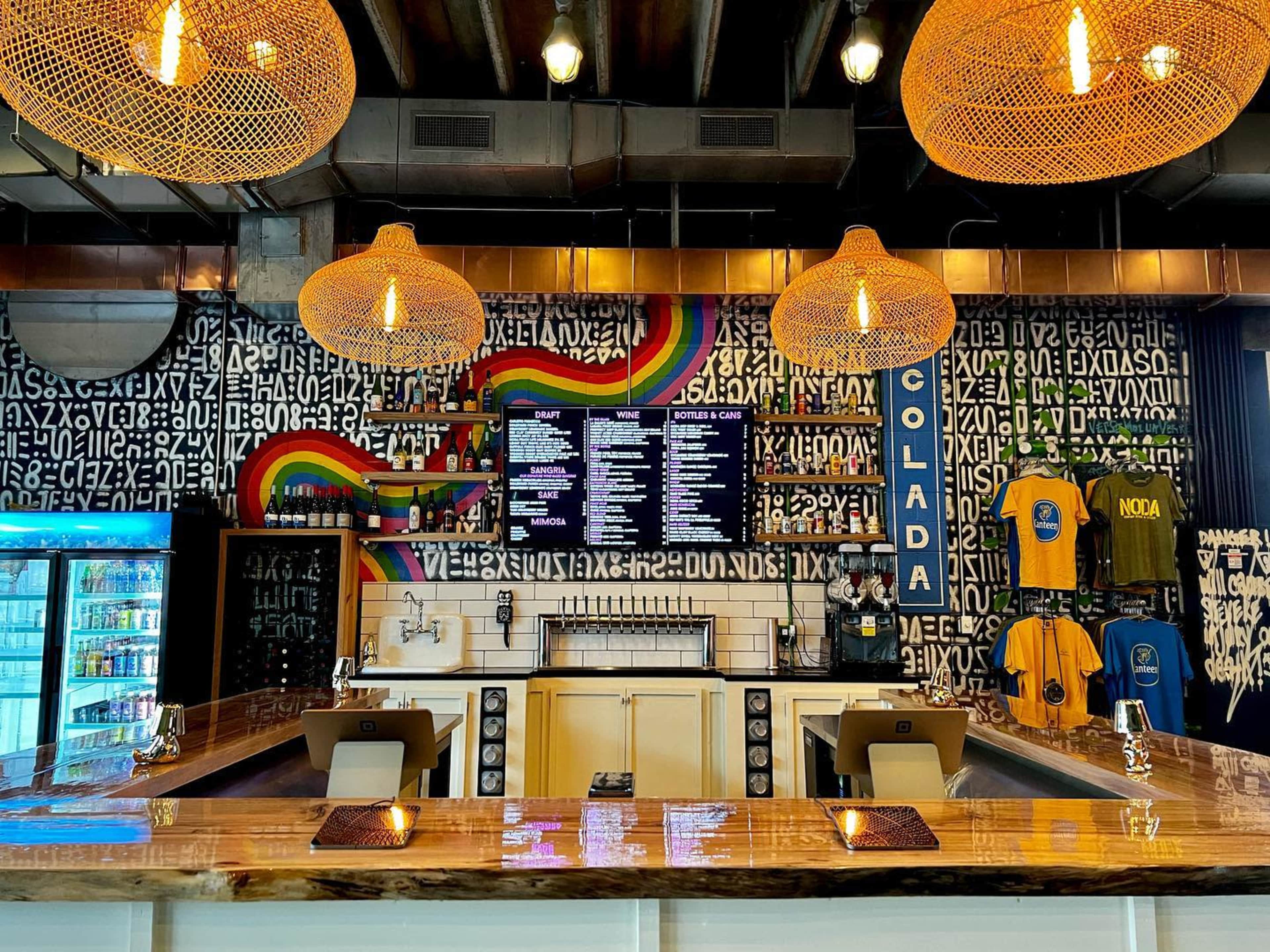 A bar with a wooden counter, a vibrant mural on the wall, and decorative hanging light fixtures.