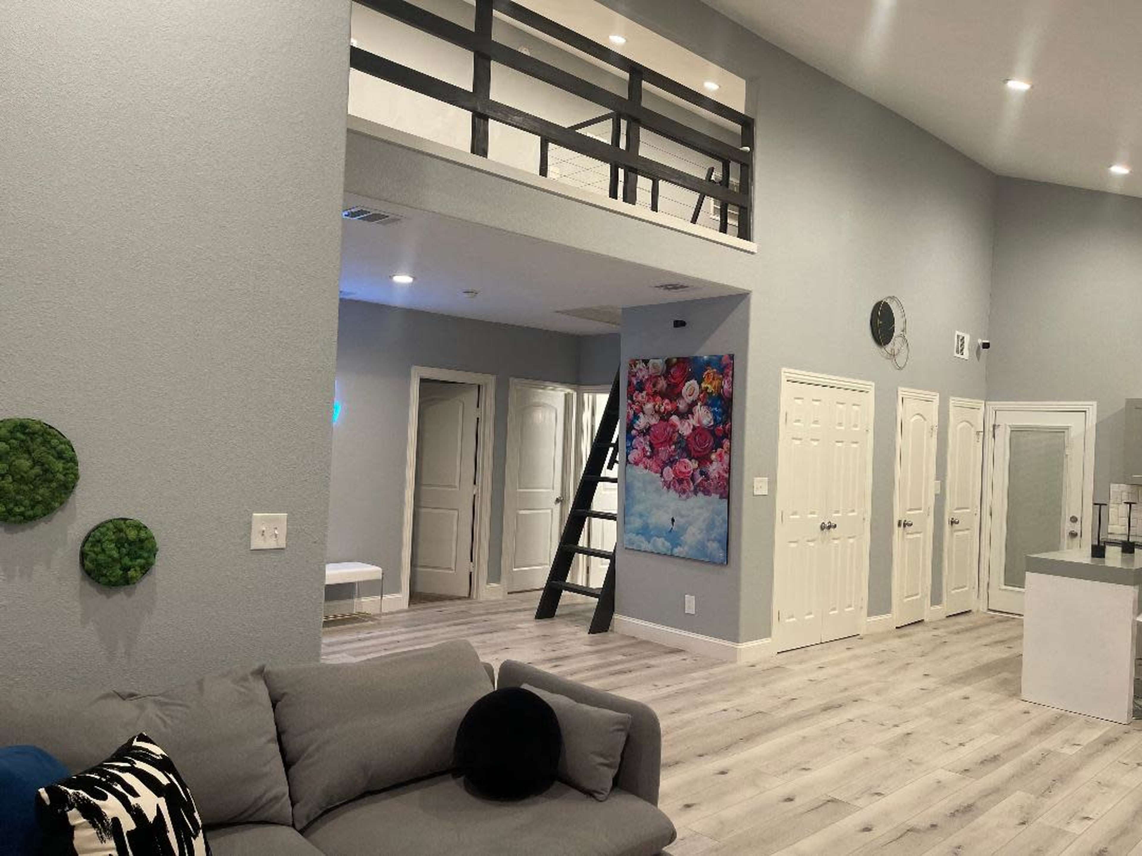 A modern living area with light gray walls, a staircase leading to a loft, and a large floral artwork hanging on the wall.