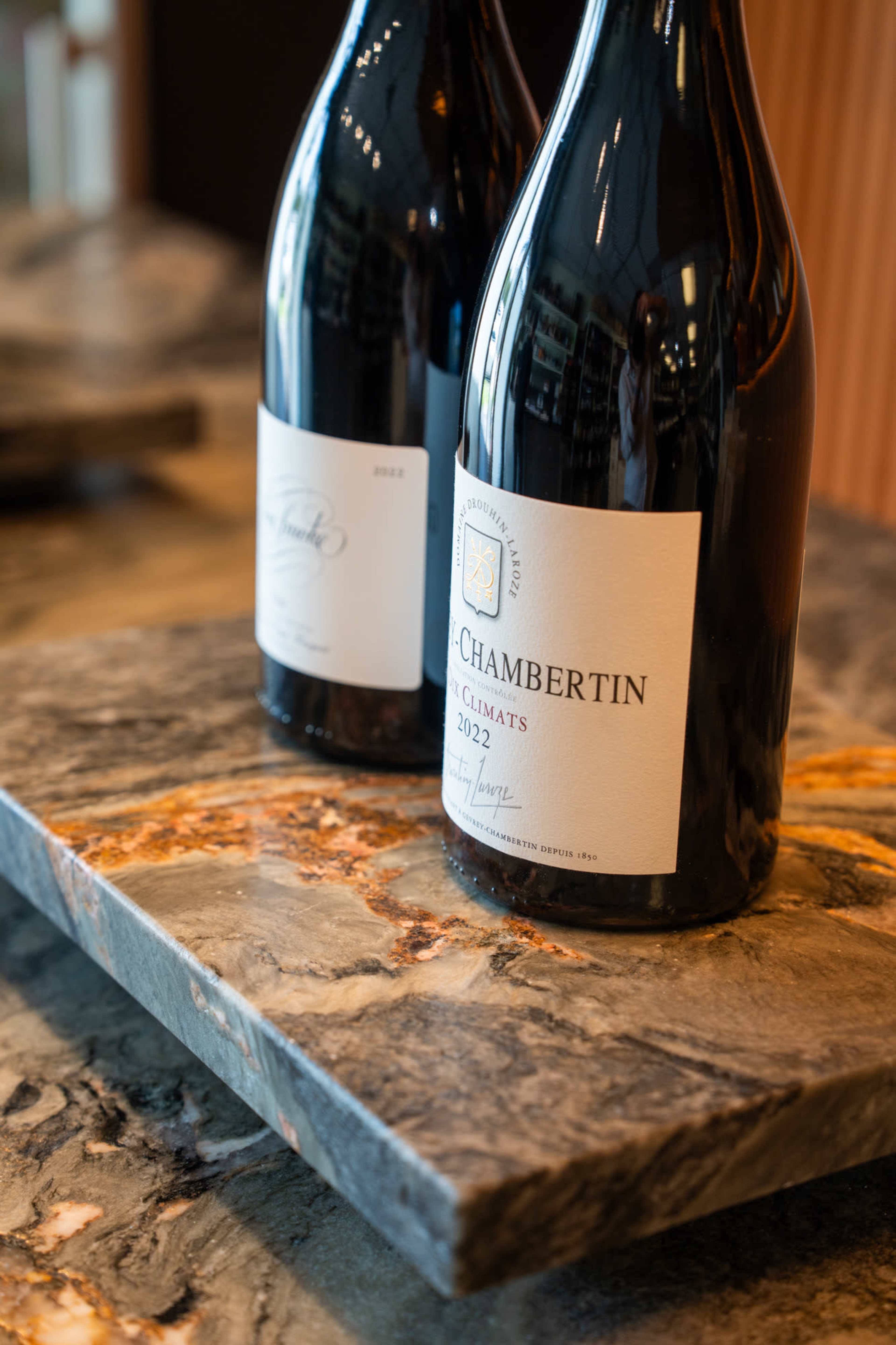 Two bottles of wine labeled "Chambetin" from the vintage year 2022 are displayed on a textured stone surface.