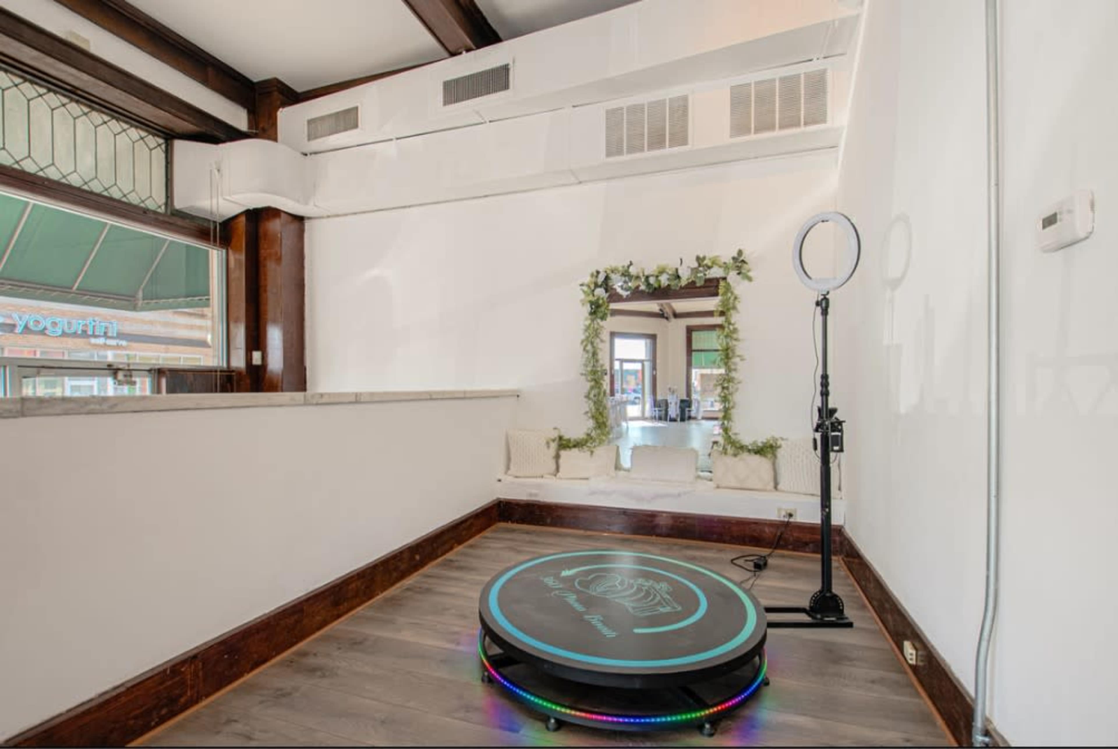 A minimalist room featuring a round platform with lights, a ring light, and a mirror framed with greenery.