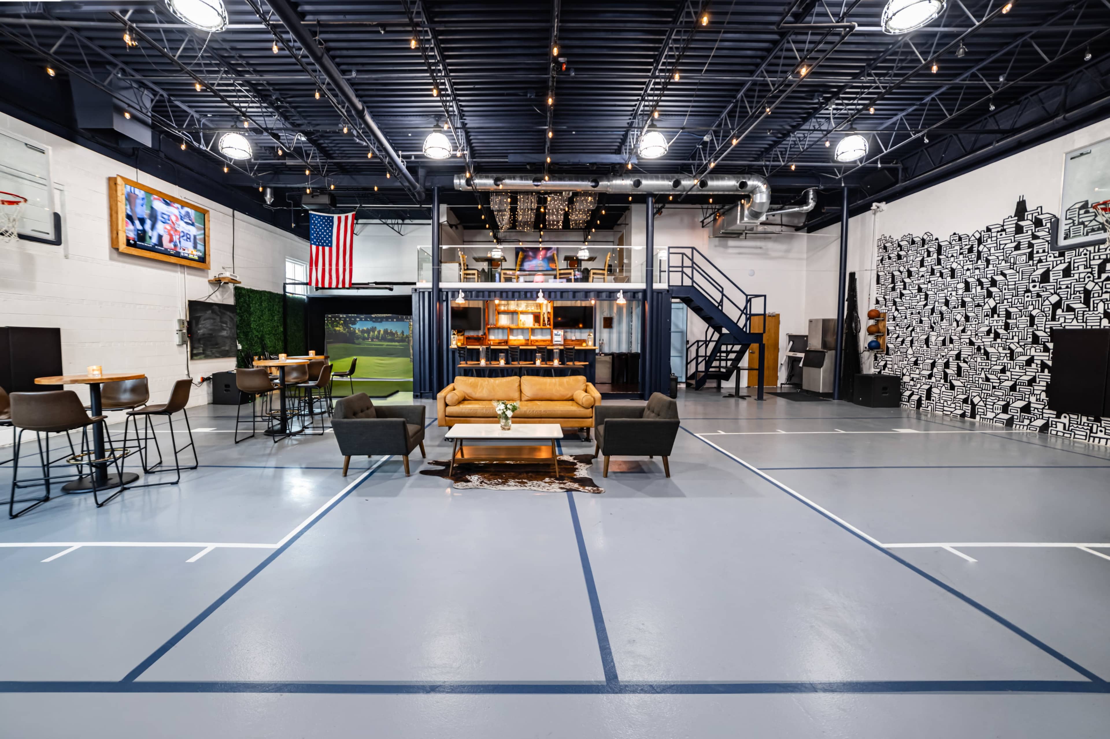 A spacious indoor entertainment area with a living room setup, bar seating, a basketball court, and an upper loft.
