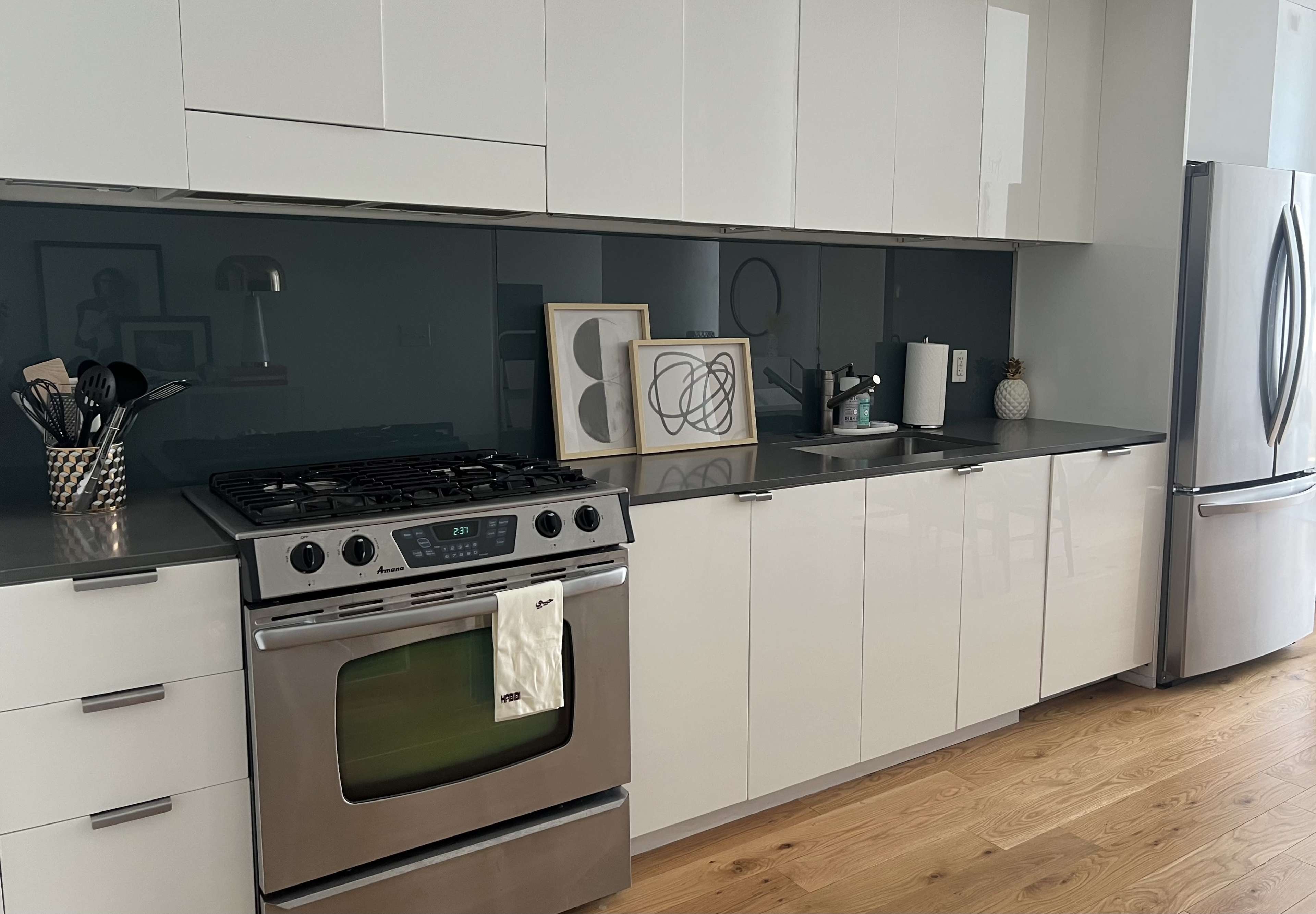 A modern kitchen features a stainless steel stove, sleek cabinets, and a dark backsplash with decorative art pieces.
