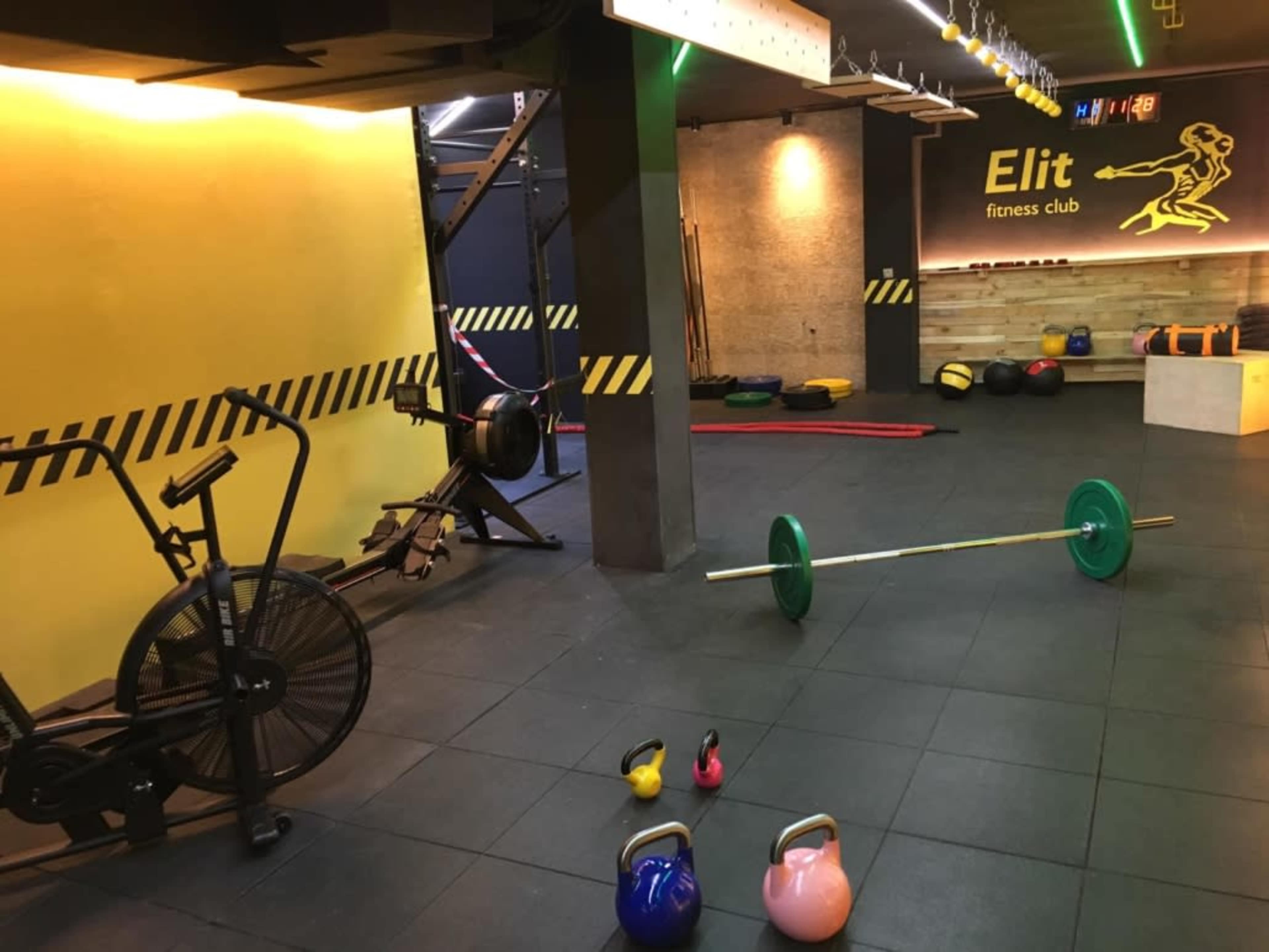 An interior view of a fitness club with various gym equipment, including kettlebells, a barbell, and an exercise bike, against a backdrop of yellow and black decor.