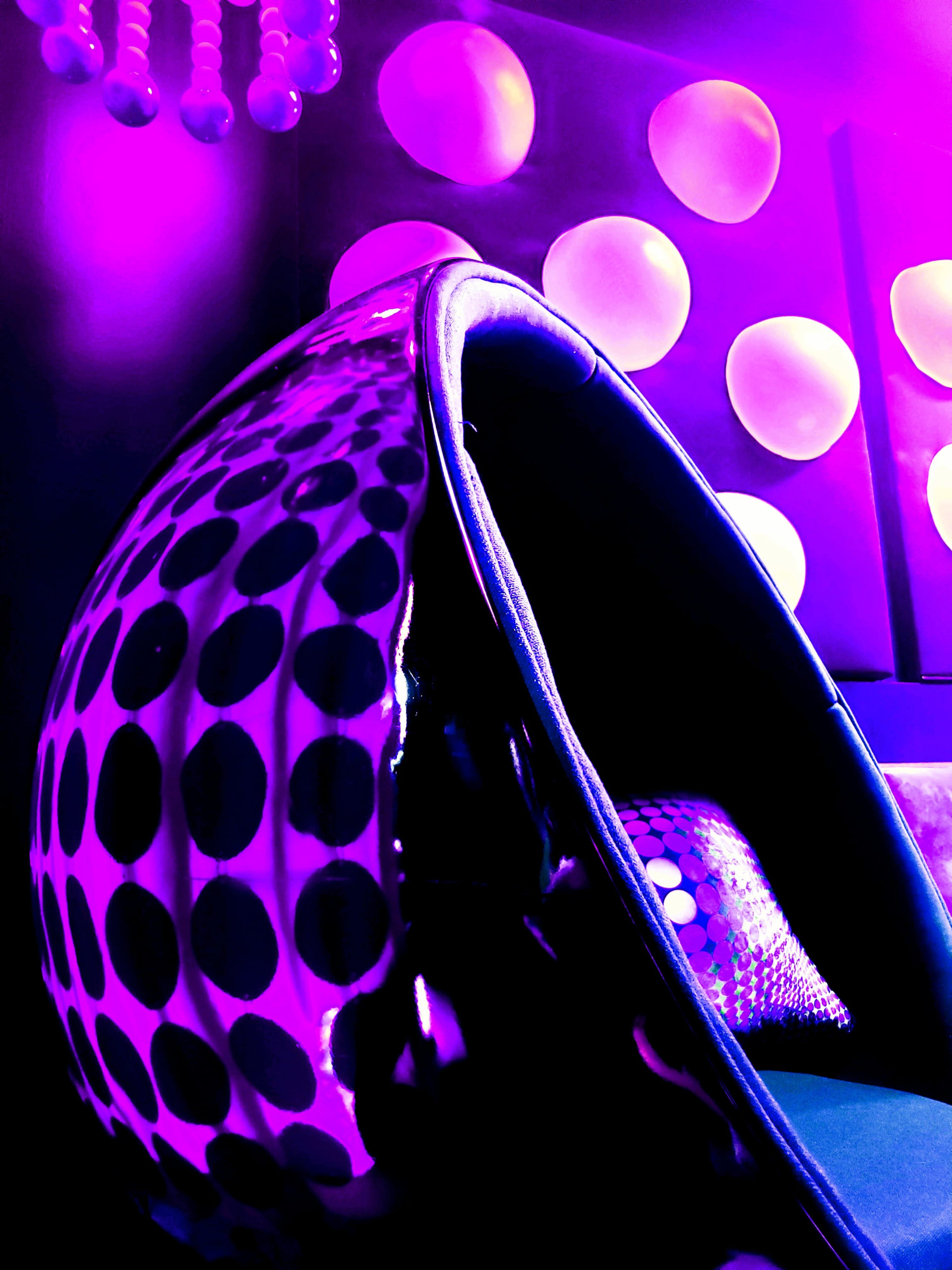 A modern, circular seat with a black and white polka dot design, illuminated by purple lighting against a backdrop of spherical wall decorations.