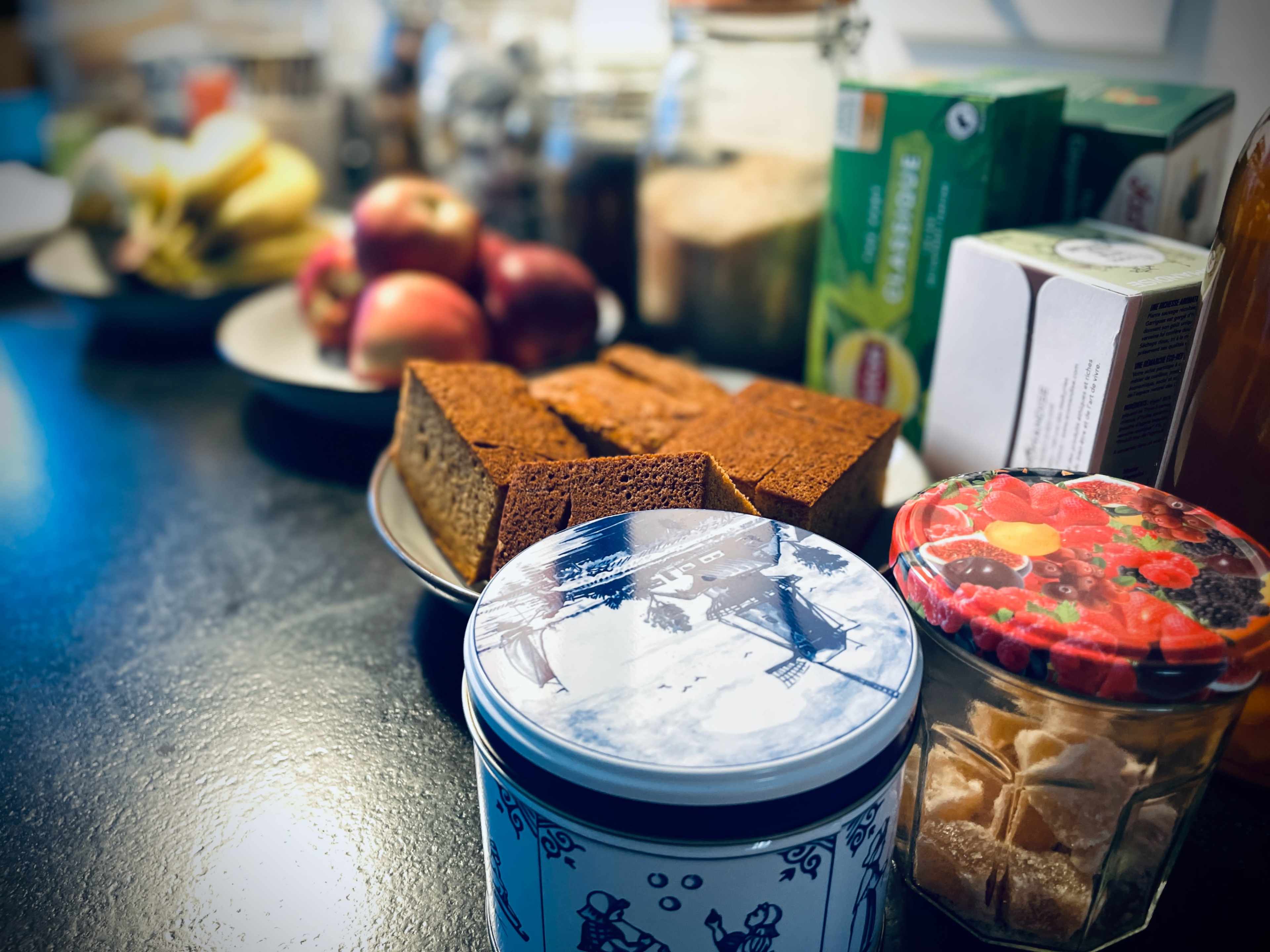 A countertop displays a variety of food items, including apples, baked goods, and jars of snacks and drinks.