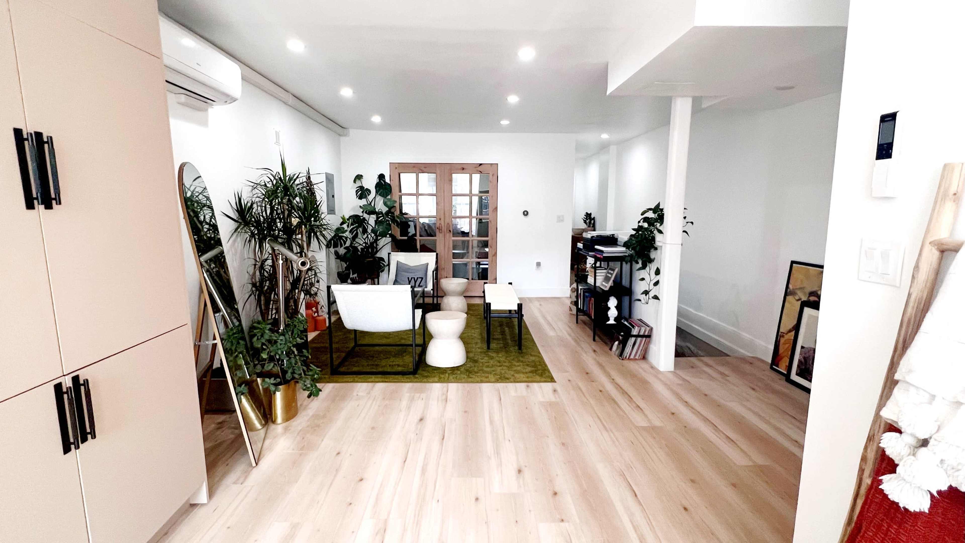 A spacious, well-lit room with modern furniture, plants, and wooden flooring.