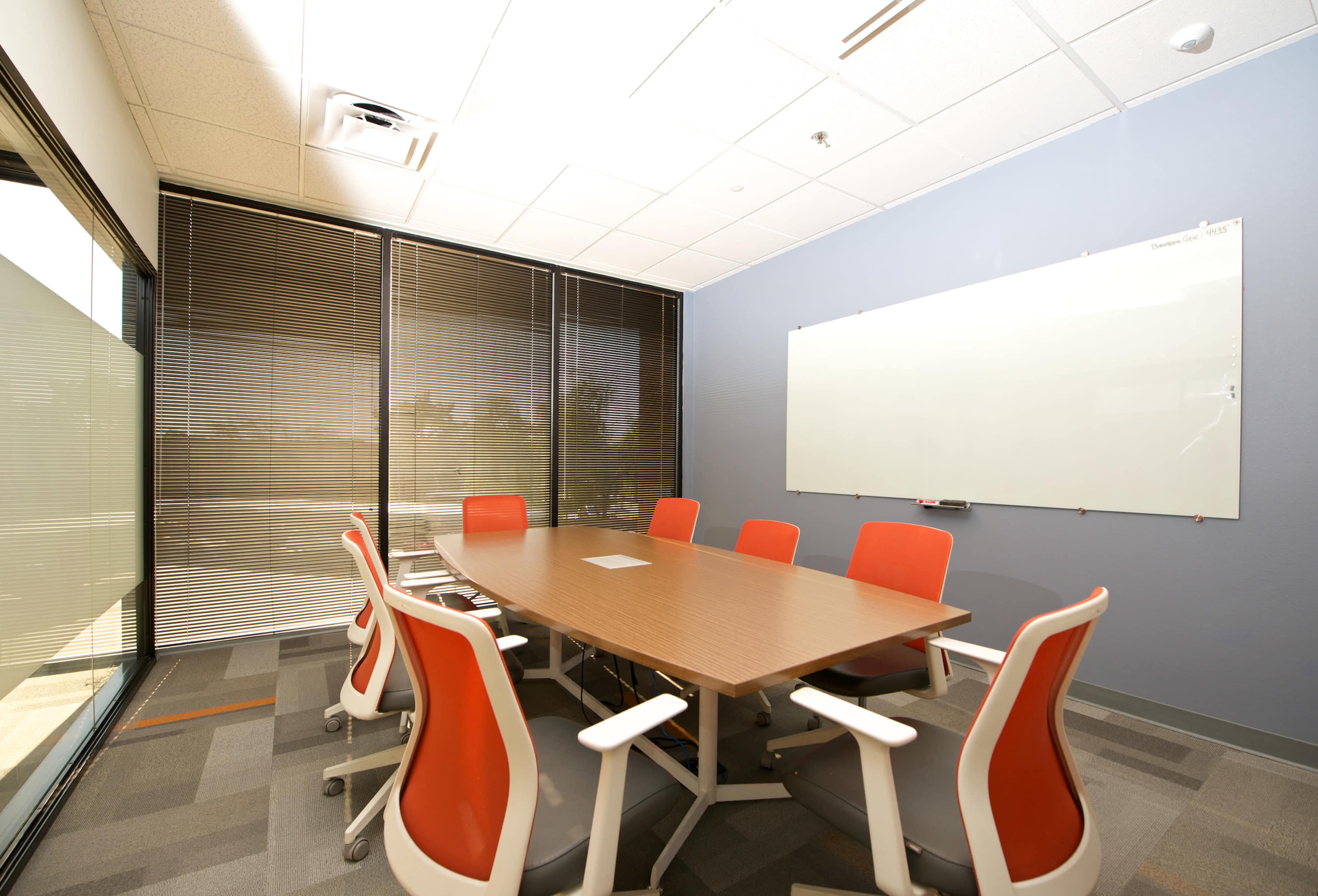 A conference room features a large wooden table surrounded by ergonomic chairs and a whiteboard on the wall.
