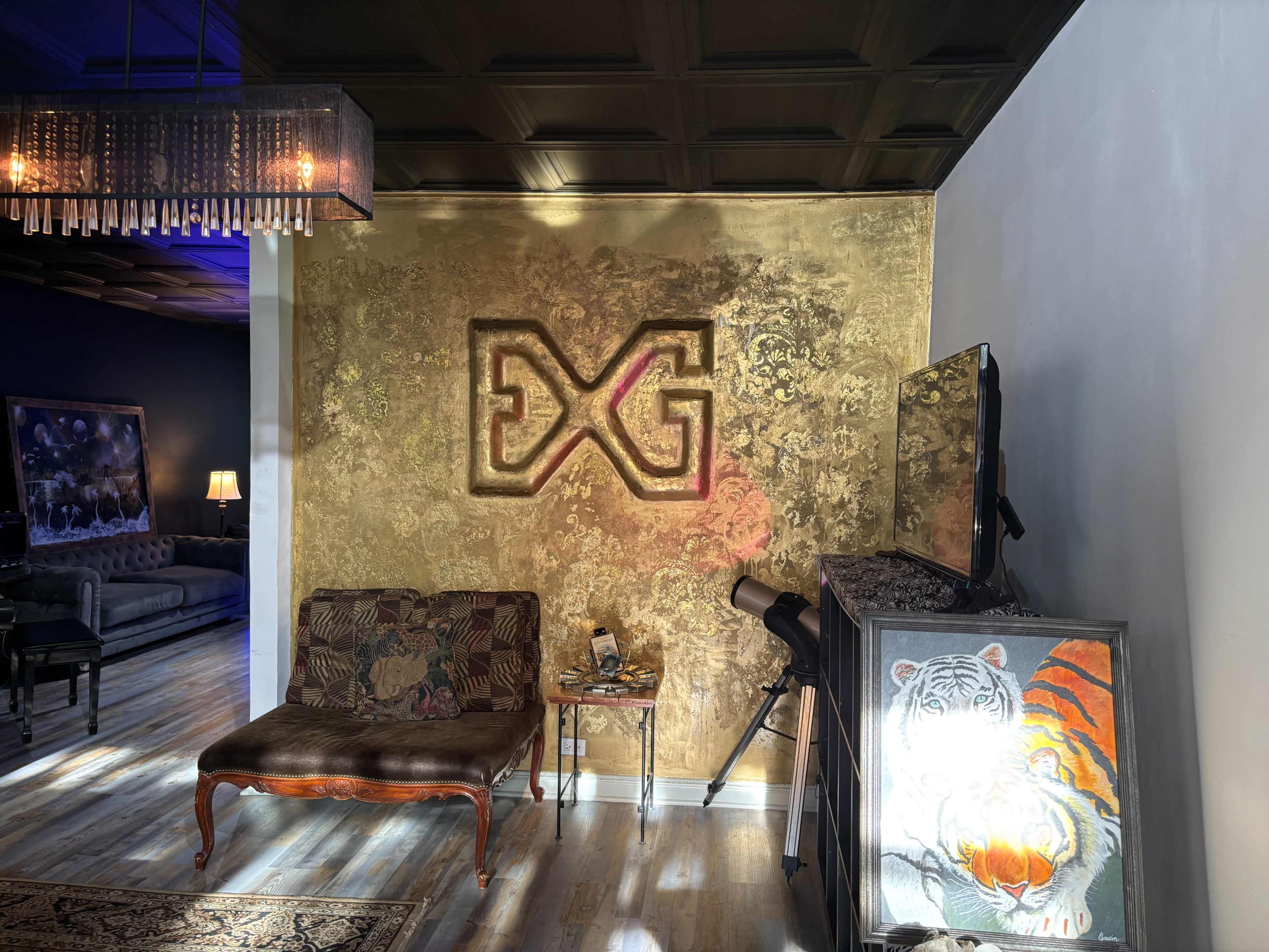 The image shows a stylish interior with gold-painted walls featuring a logo, a vintage couch, a telescope, and a framed artwork of a tiger.