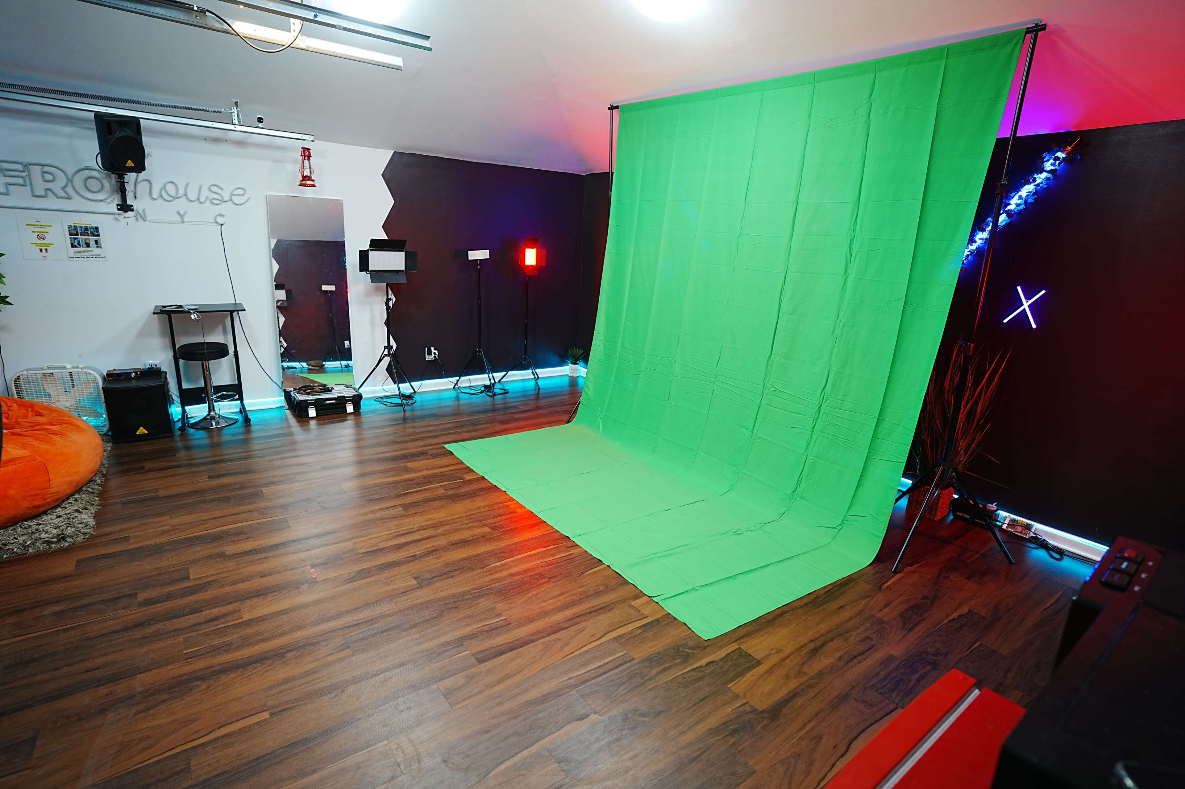 The image shows a studio setting with a green backdrop on a wooden floor, illuminated by various lights and featuring a small table with equipment in the background.