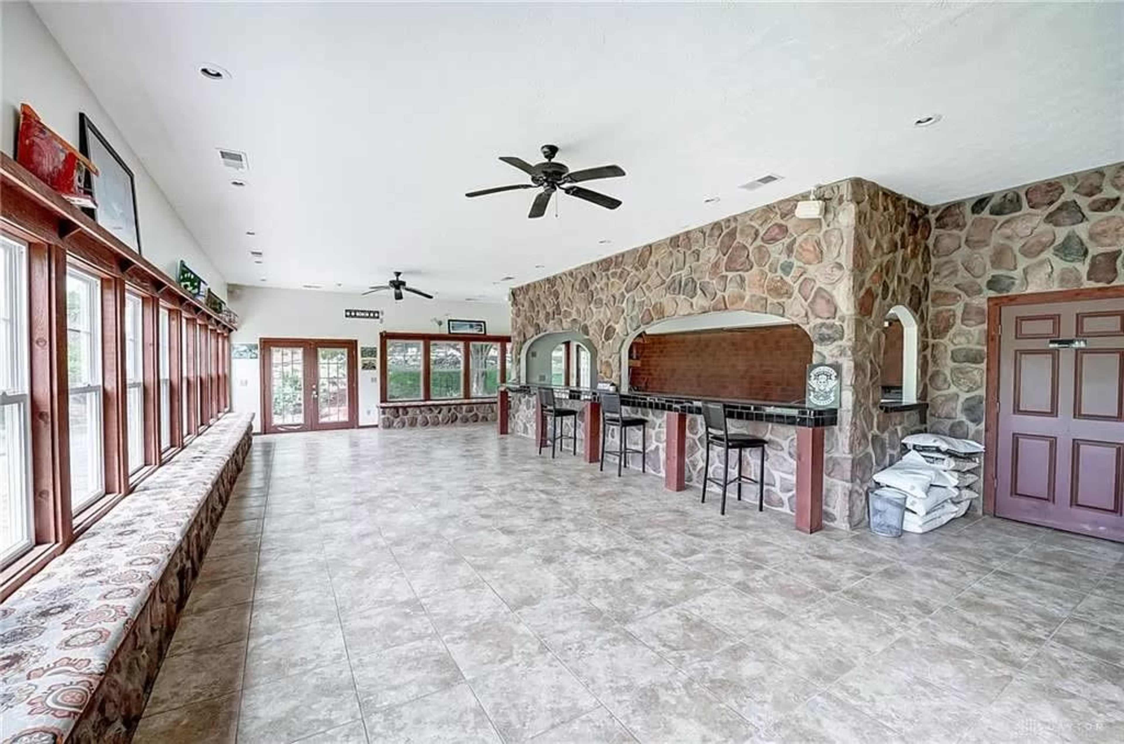 A spacious room with stone walls, a large bar area, and numerous windows allowing natural light to enter.