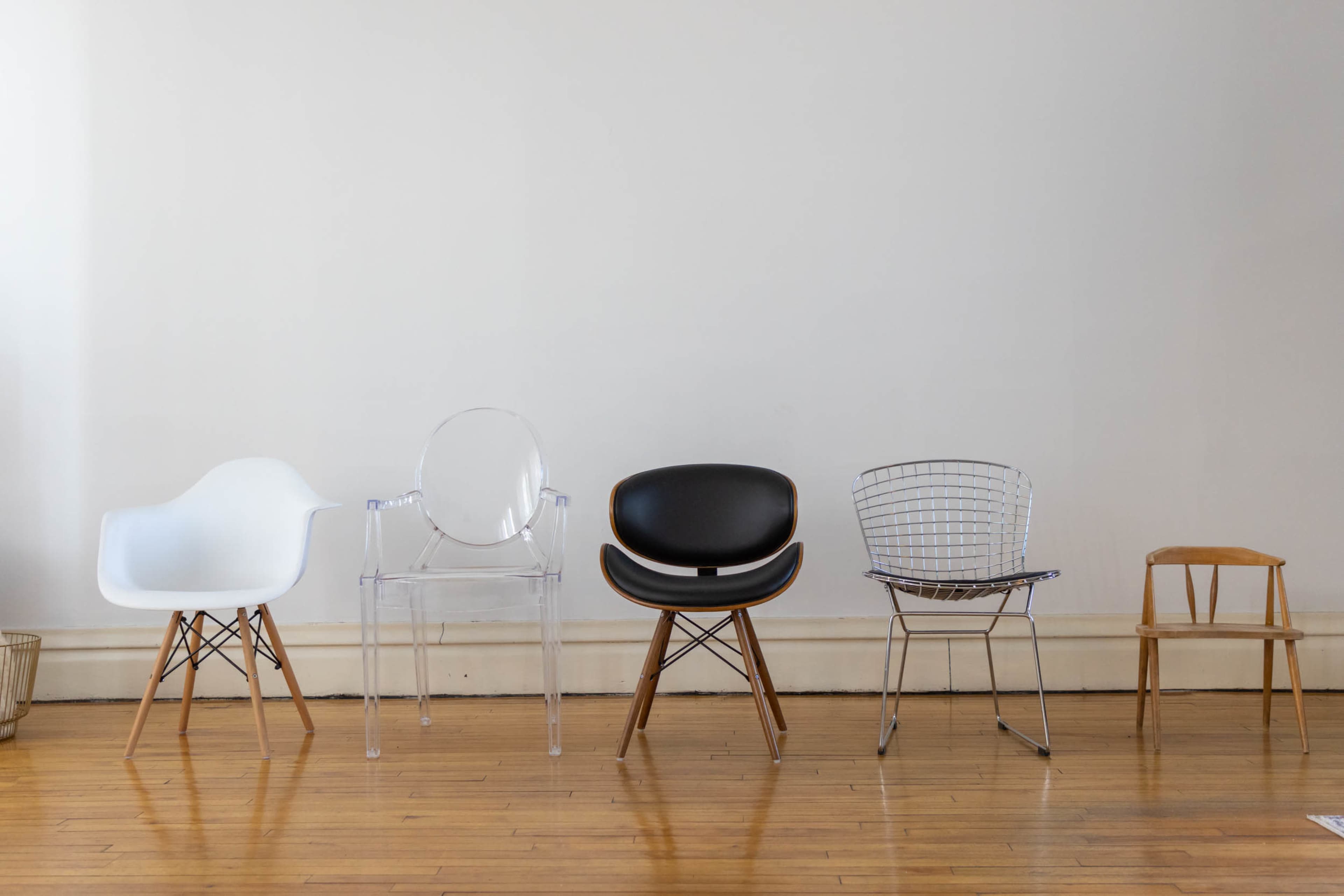 The image depicts five distinct chairs lined up against a plain wall, showcasing a variety of designs and materials.