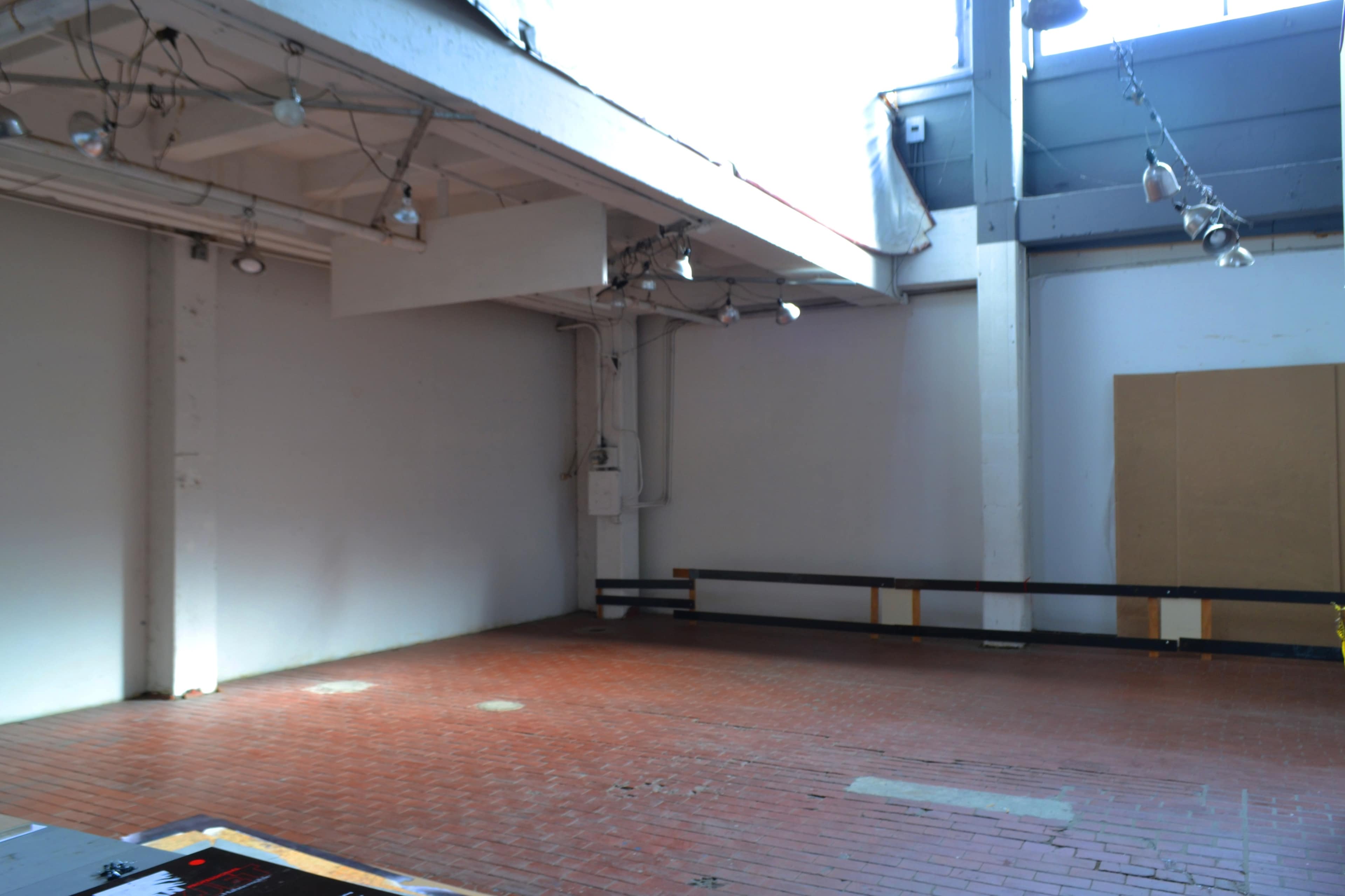 An empty room with a brick floor and high ceilings, featuring exposed beams and overhead lights.